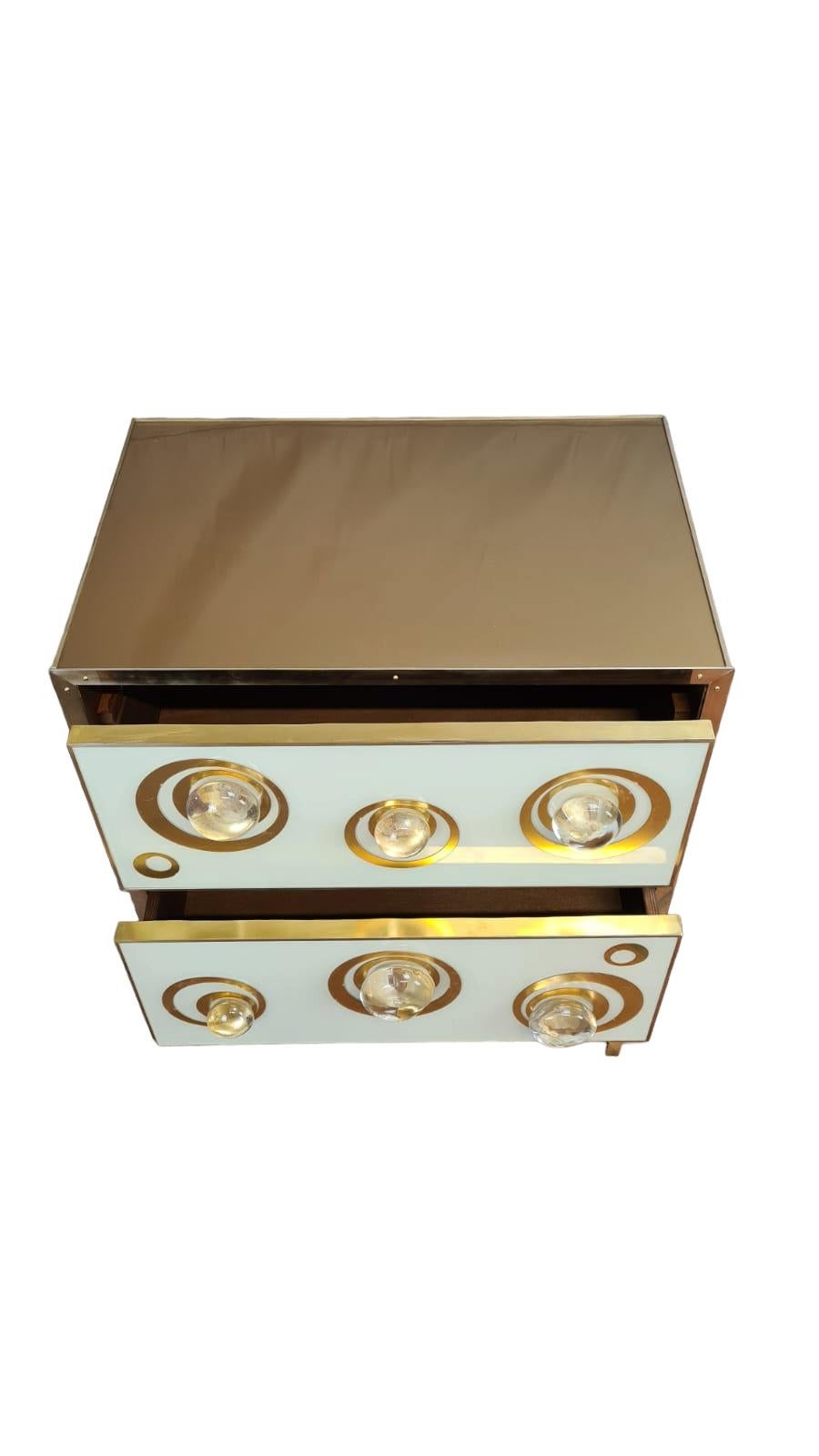 Imagina que entras en una habitación decorada con gusto y te fijas inmediatamente en dos preciosas mesillas de noche blancas y doradas que llaman la atención por su refinada elegancia.  

Los cajones de la mesilla de noche están hechos de fusión de
