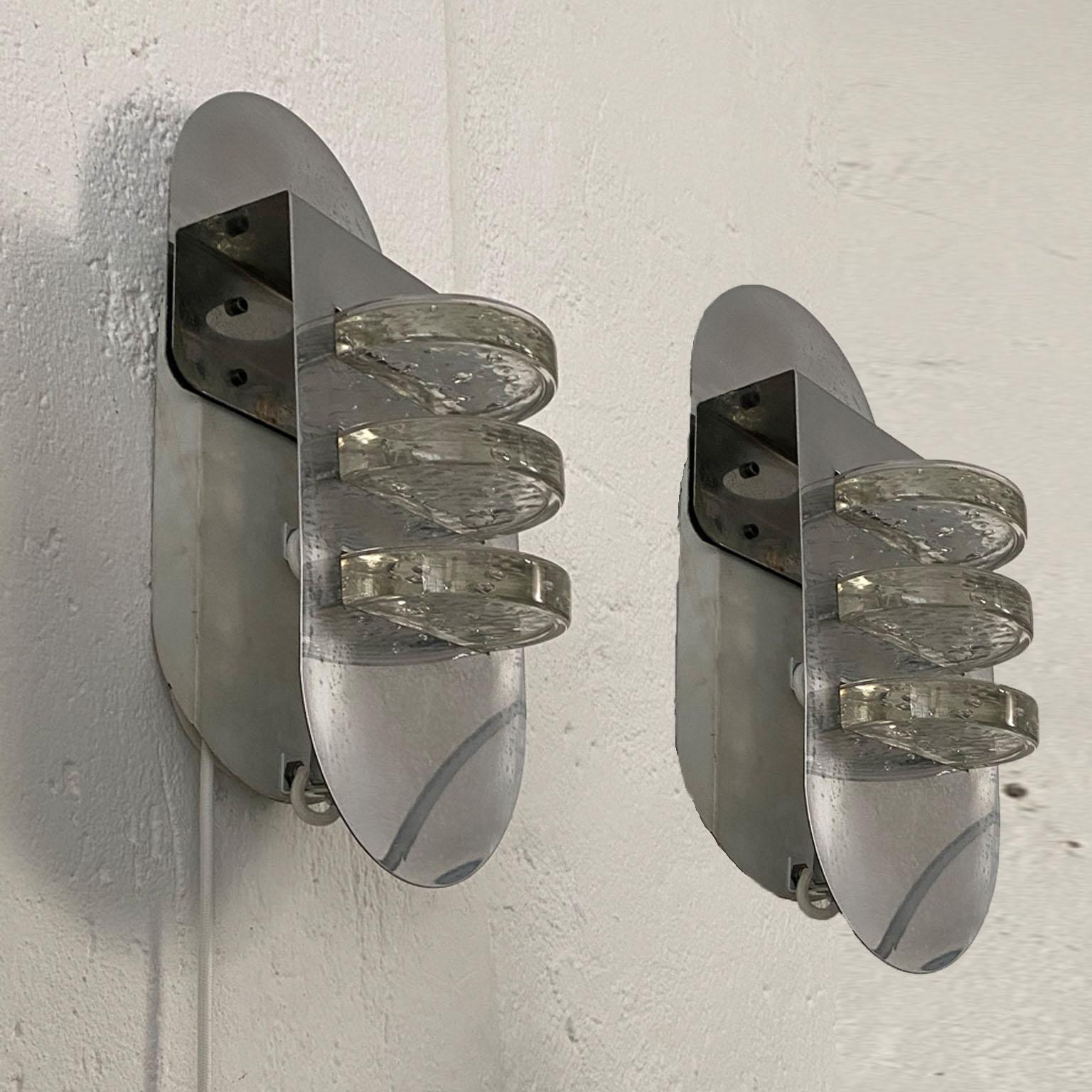 This is a rare pair of anonymous yet very fascinating wall sconces from the 1970s. Crafted in chromed metal and corrugated Murano glass, each lamp holds three transparent glass discs with included bubbles. The light effect is very peculiar, thanks