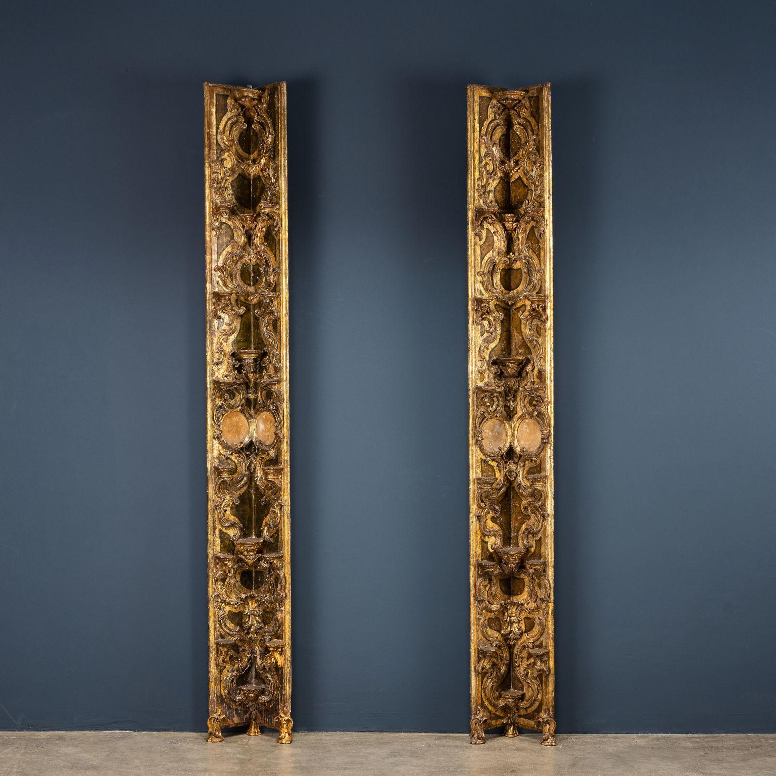 Pair of carved corner pilasters holding a porcelain collection; supported by three carved feet, they develop on the entire surface a carving with leafy curls and flowers that act as a support for the shelves or as a support with a curl for the