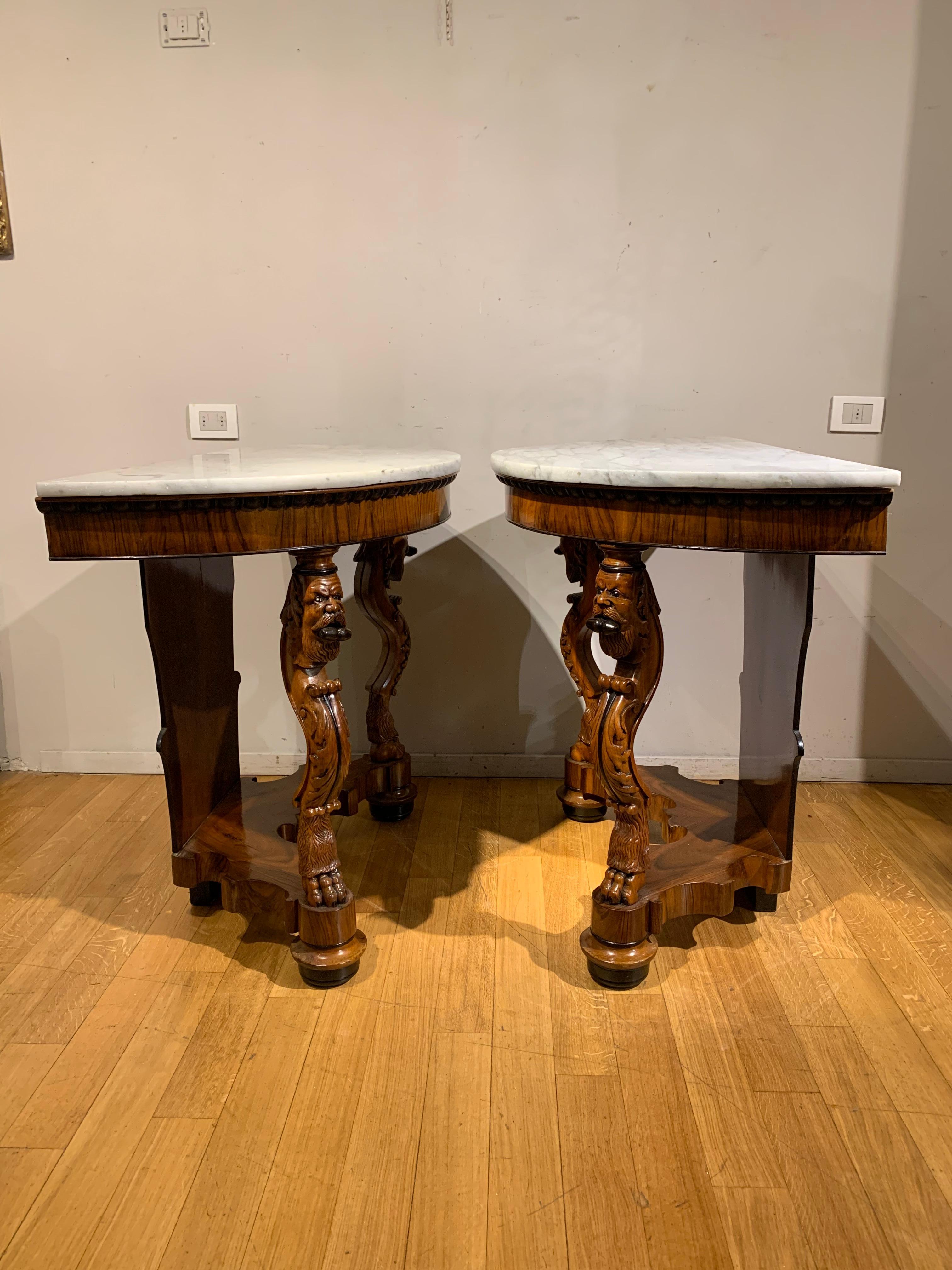 Elegant pair of consoles in mahogany and walnut with carved and partially burnished details.
With a half-moon shape, these two pieces of furniture are supported by two legs carved in the shape of fantastic animals and a wooden base with a zither