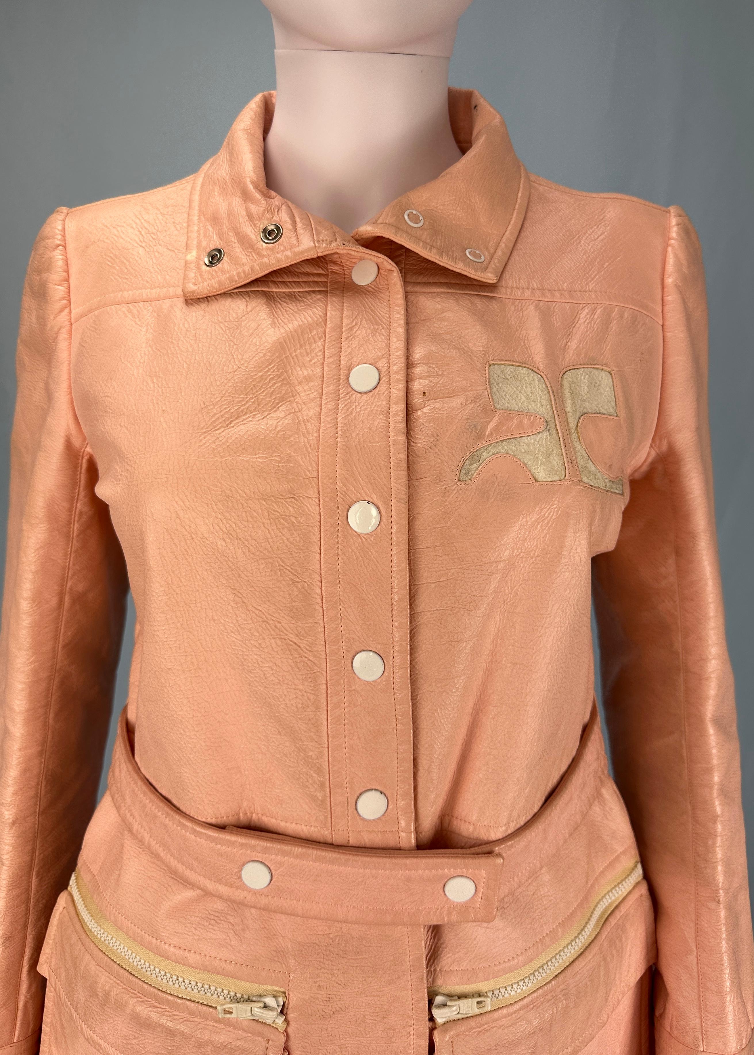 Vintage Courrèges 
1963-1969

Veste en vinyle rose pêche 
Grand logo Courrèges 
Peut être porté comme une veste ou une robe
Ceinture (amovible) 
Boutons de fermeture

Label couture numéroté 
Taille 