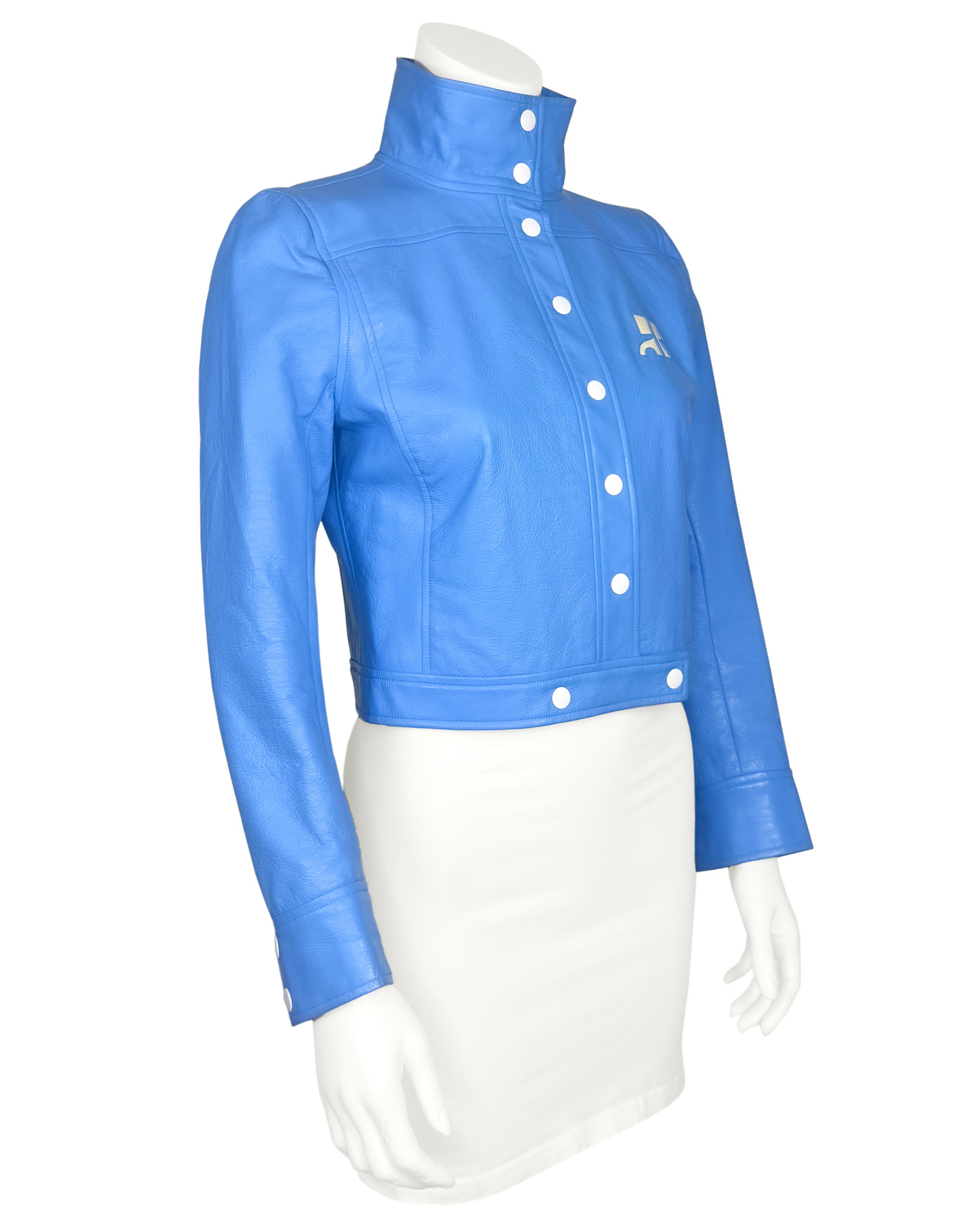 Veste d'occasion en cuir vinyle bleu Courrèges avec col cheminée, logo crème sur la poitrine, manches longues avec poignets boutonnés, coupe boxy et fermeture par boutons pression. Doublure logo.

Très bon état, très peu de signes d'usure

Label
