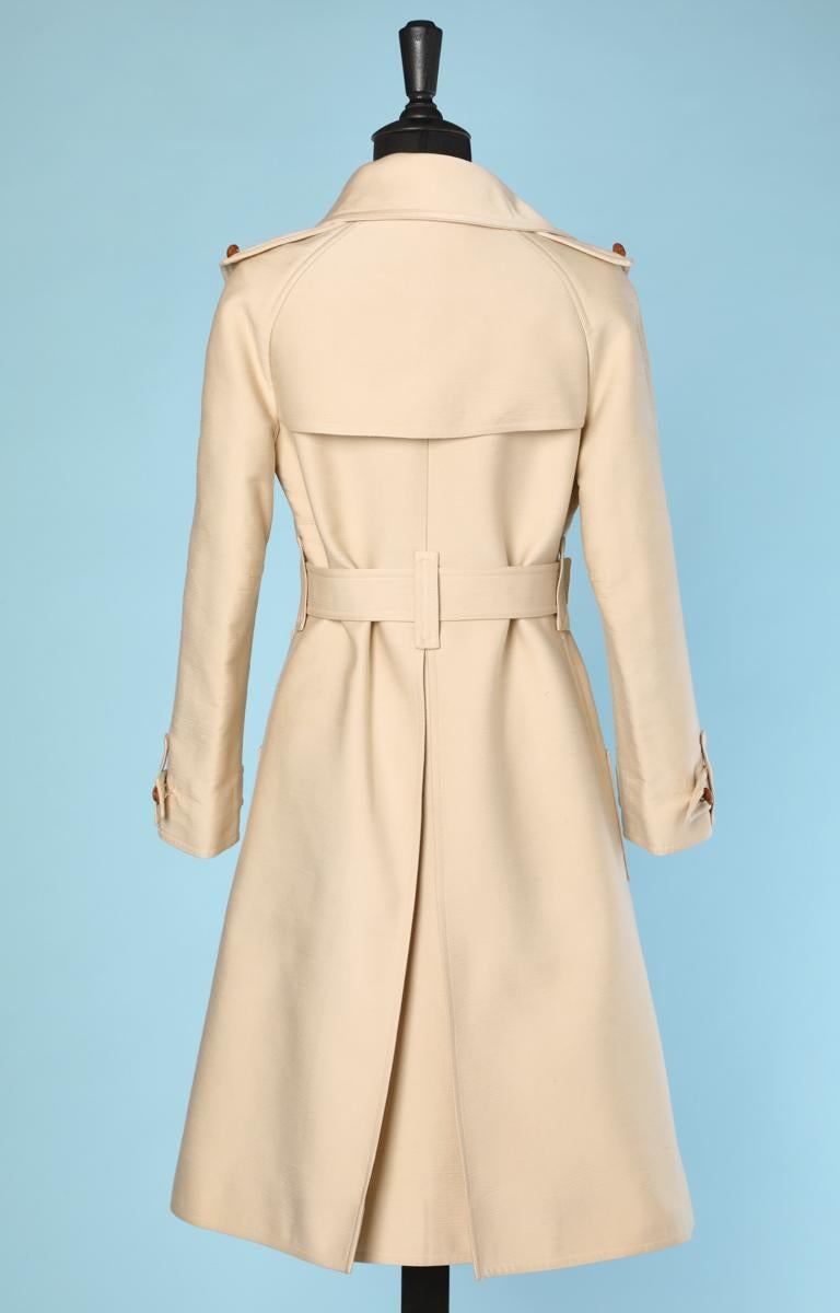 Trench coat in thick ecru cotton, leather buttons, belt, beige zip, buttoned tabs on shoulders, buttoned pockets, buttoned tabs at the bottom sleeves, open back pleat, white monogrammed yellow silk lining and Courrèges 1970 Courrèges Paris label