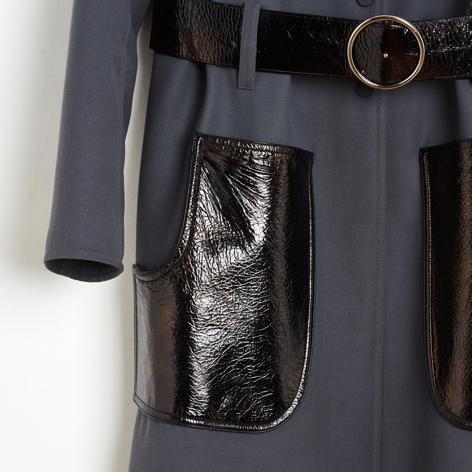 Courrèges trench coat in gray wool gabardine, high collar closed by 7 matching snaps up to the waist, equipped with belt loops and a wide belt with pin buckle to close on the waist, 2 large pockets in contrasting black vinyl (each with an additional