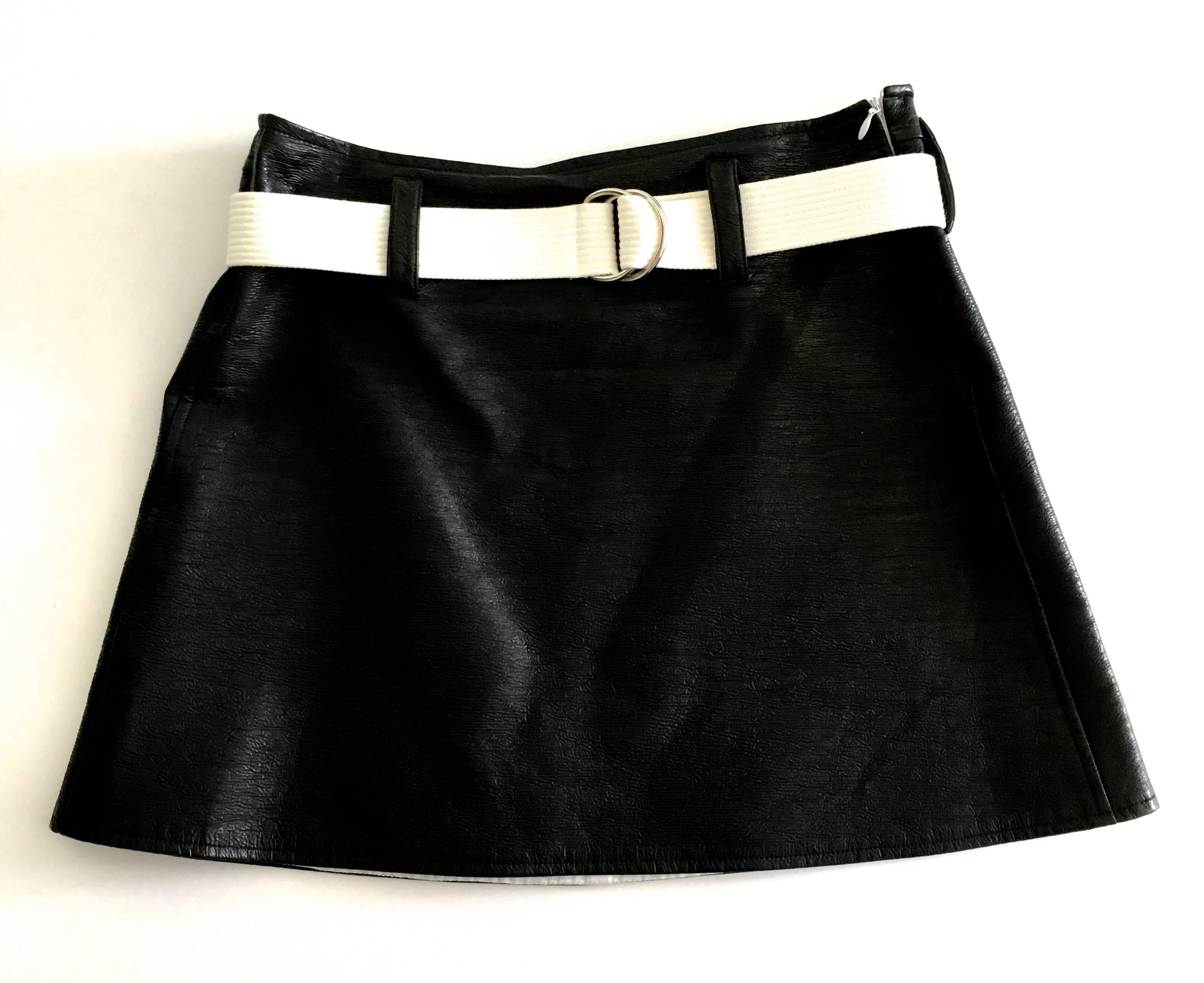 Presented here is a sultry mini skirt by Courreges Paris from the 1980's. This iconic mini skirt is made from black patent leather with white trim. The skirt is fully lined. The skirt has a gorgeous white fabric belt with it that is size adjustable.