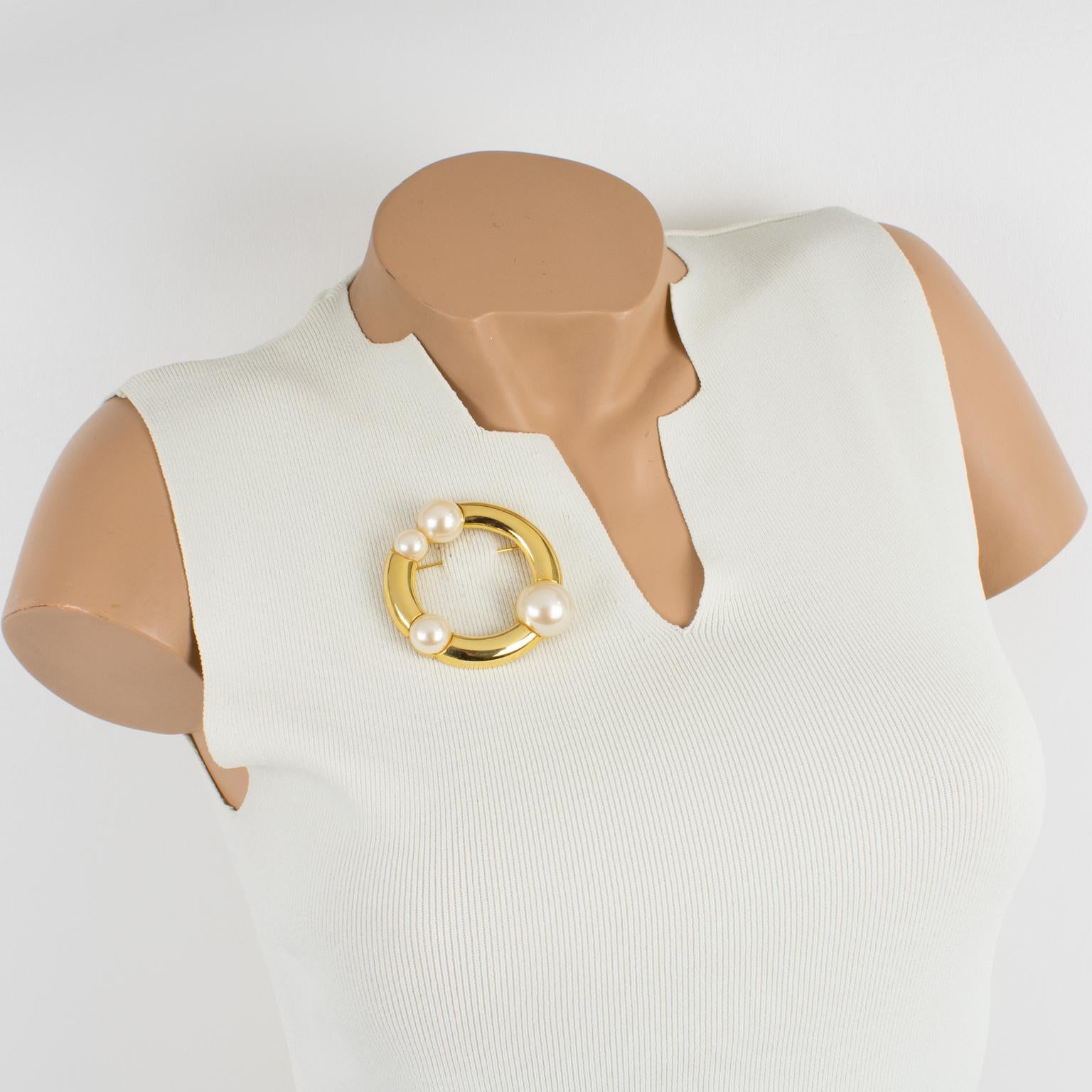 This elegant Courreges Paris modernist pin brooch features a dimensional and rounded donut shape, with shiny gilt metal ornate with pearl-like half beads in assorted shapes. The pin has a security closing clasp and is signed on the underside with