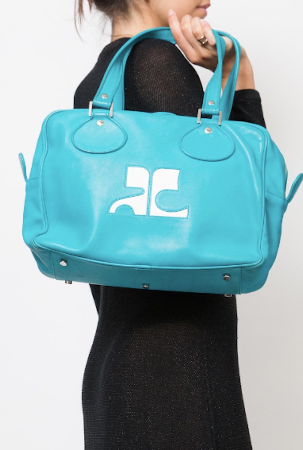 Courreges turquoise large Bowling handbag featuring two top handles, silver-tone hardware, a large front white logo inside zipped pocket, an inside logo patch. 
Circa: 2000s
Length: 13.4in. (34cm)
Height: 9.4in. (24cm)
Depth:4.3in. (11cm)
In good