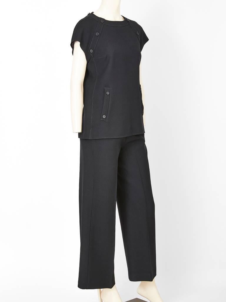 André Courrèges black, wool gaberdine, tunic and pant ensemble. Top has a capped sleeve, jeweled neckline with a semi fitted waist and then flares out in an A line shape. There are vertical button embellishments on both sides of the tunic. Pant is