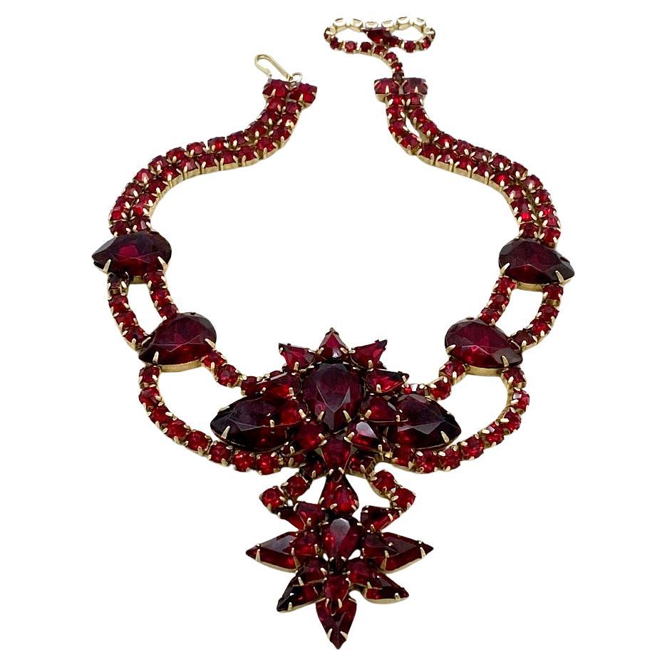 Dies ist eine luxuriöse Halskette mit rubinroten Strasssteinen im Court-Stil. Diese Doppelkette mit Anhänger besteht aus birnen-, tropfen-, quadrat- und rundförmigen Strasssteinen. Alle Strasssteine in Zackenfassung auf kupferfarbener