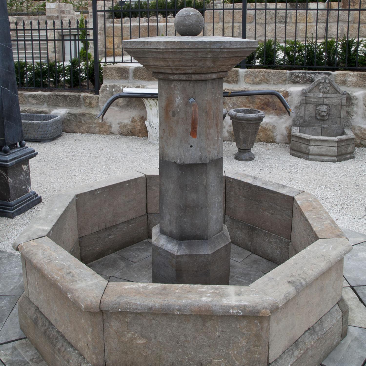 Octagonal fountain out of hand-carved natural stone, with an octagonal column, large capital with ball on top and four spouts (Dimensions of Column: 160 x Ø67 cm). The basin has a height of 50 cm and a diameter of 163 cm. Together with the baseplate
