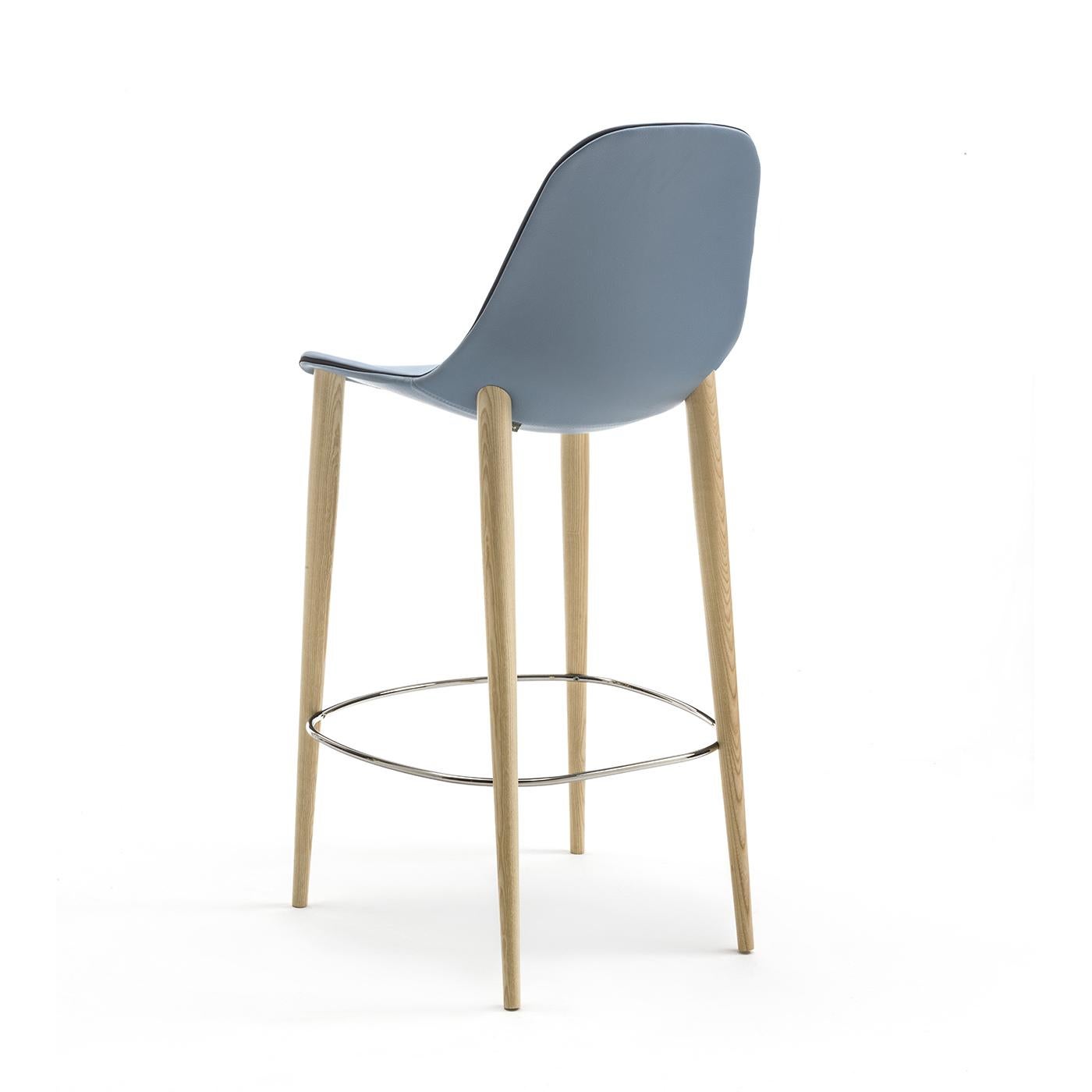 Le design minimaliste de cette chaise la rend parfaite pour tous les environnements. Sa structure est composée de quatre pieds fixes en bois de frêne naturel et d'un repose-pieds chromé brillant. Sa coque en aluminium est recouverte de cuir souple