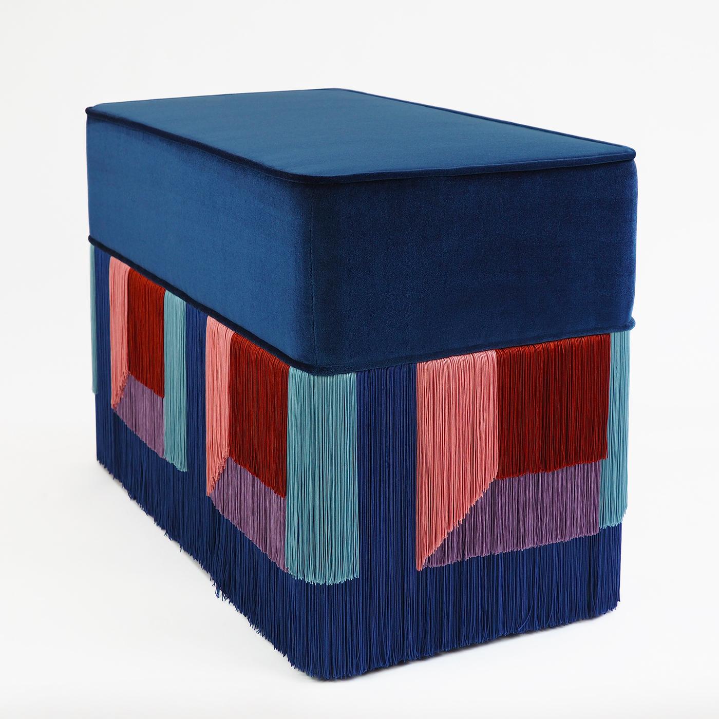 With its intense, electric blue velvet cushion, this Art Deco-inspired pouf boasts a soft feel to be shared with a beloved one. Geometric patterns of red-brick, light-blue, peach-pink and lilac fringes that meet each other in rectangular shapes,