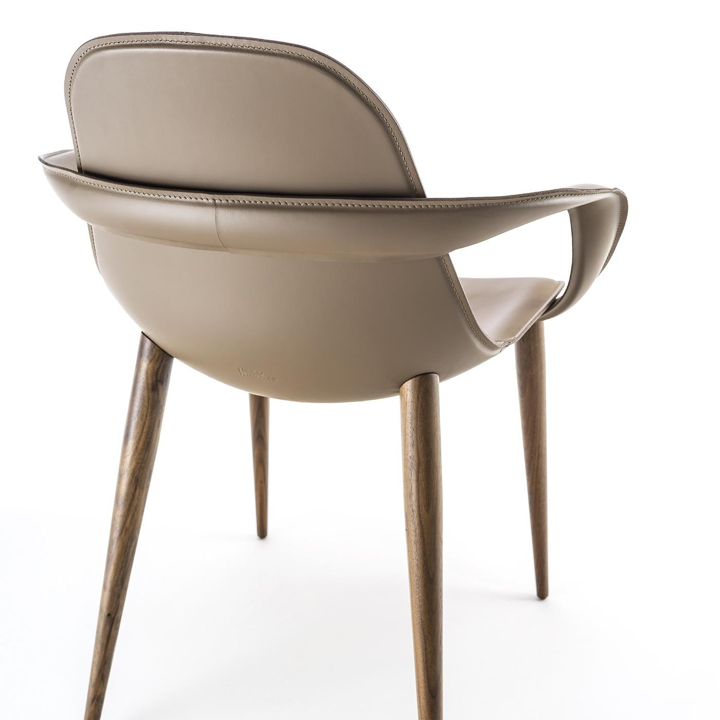 This chair was designed to fit perfectly into any space. The seat's shape holds up the back, ensuring comfort, while four Canaletto-walnut legs support the structure. The shell is in aluminum, covered in soft, taupe leather. Ribbon-shaped armrests