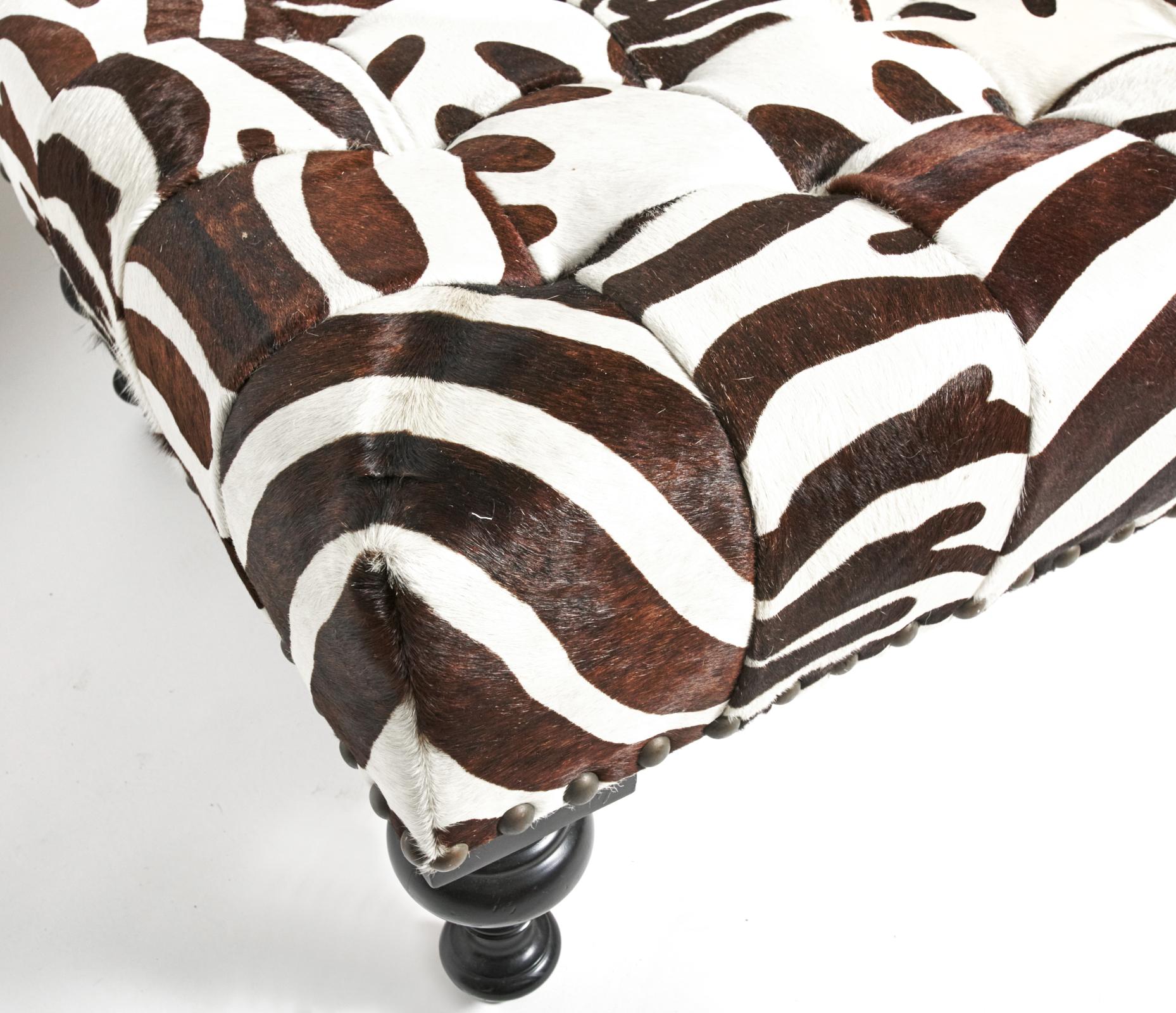 Stylish large coffee table size ottoman covered in cowhide and dyed in a zebra pattern which has been patch worked together. Tufted top in excellent condition. 4 turned wooden legs. Measures: 48