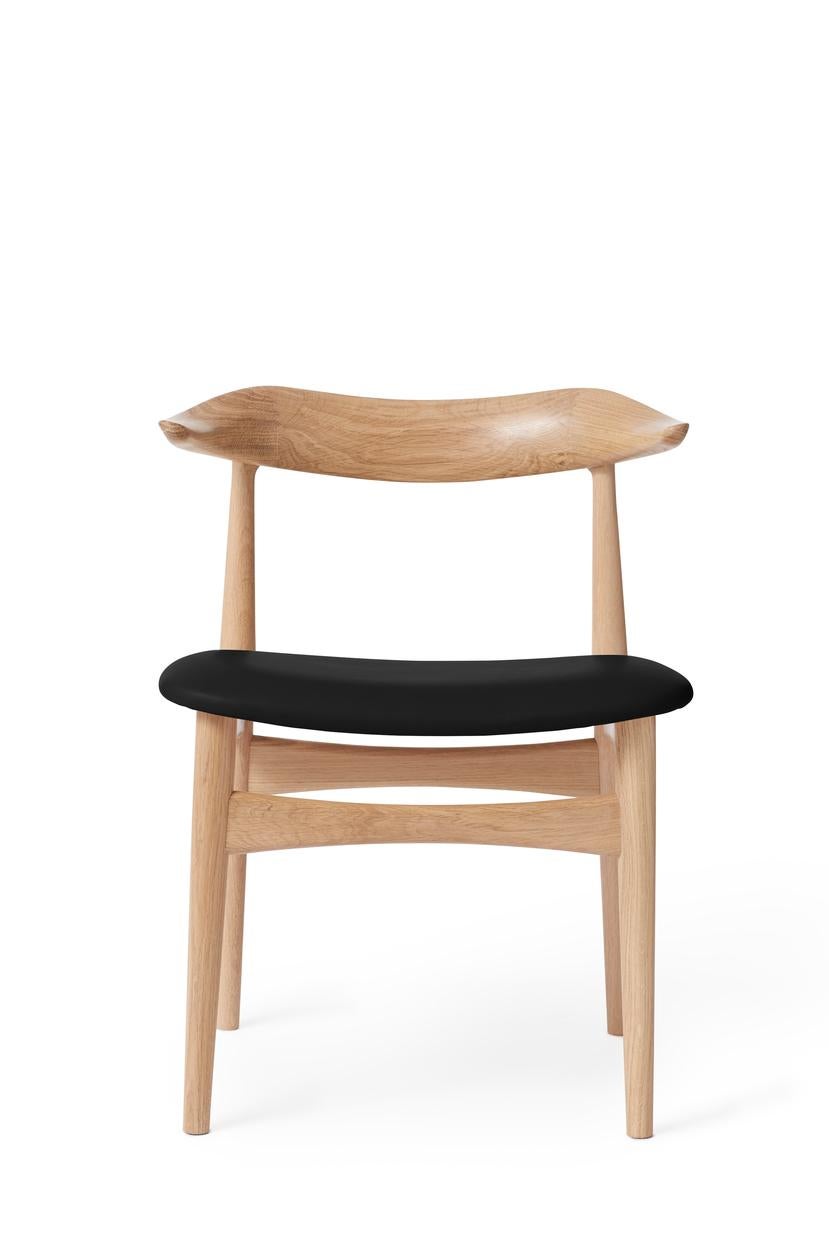 Cow horn chair oak black leather by Warm Nordic
Dimensions: D55 x W48 x H 74 cm
Material: white oiled solid oak frame, textile or leather upholstery.
Weight: 7.5 kg
Also available in different colours and finishes. 

The Cow Horn Chair is an