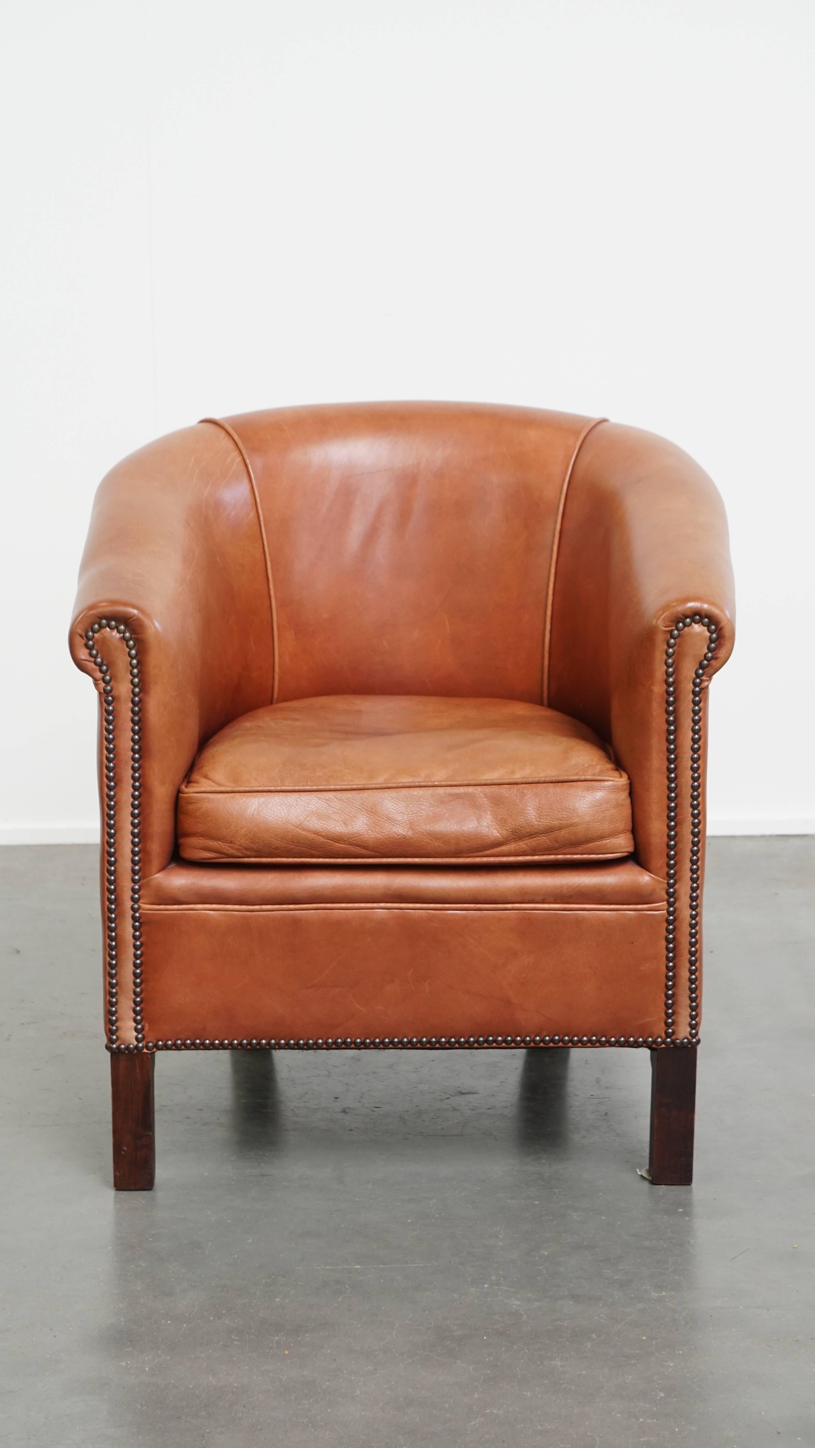 Questa poltrona da club in pelle di vacchetta ben conservata è di colore cognac chiaro. Questa poltrona club in pelle color cognac chiaro si integra facilmente in interni sia classici che moderni, aggiungendo quel tocco di carattere ed eleganza in