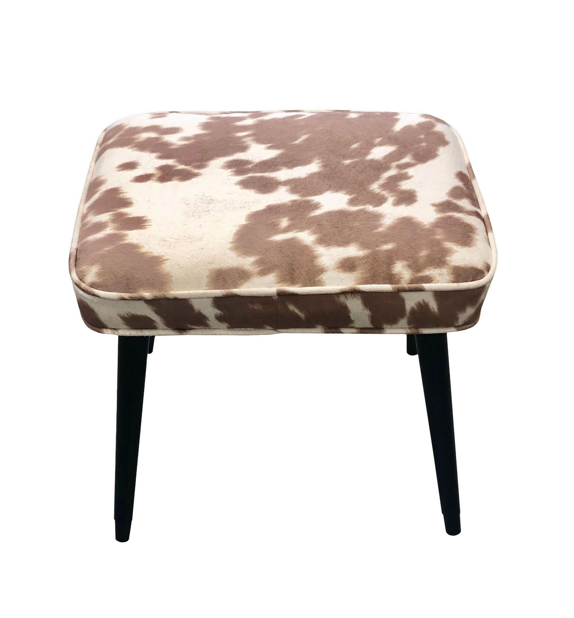 A rectangular mid century stool. Black lacquered wooden legs with gold tips. Upholstered in cowhide suede. Circa 1950s.