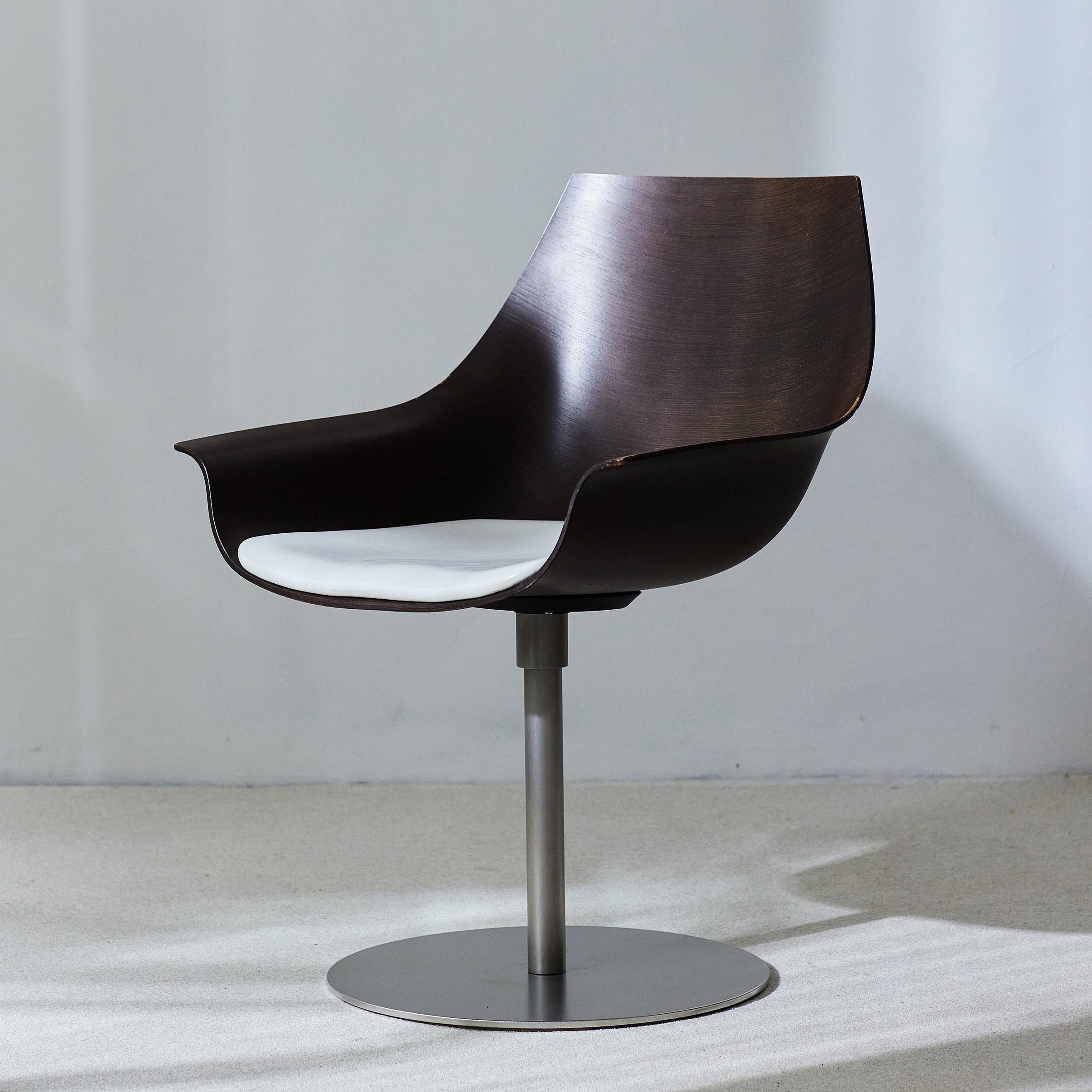 Fauteuil pivotant avec une coque incurvée en placage de bois - modèle COX conçu par Ostwald et Nolting pour LaPalma - doté d'une assise en cuir blanc et monté sur un piètement circulaire en acier inoxydable. Les deux designers ont rendu hommage aux