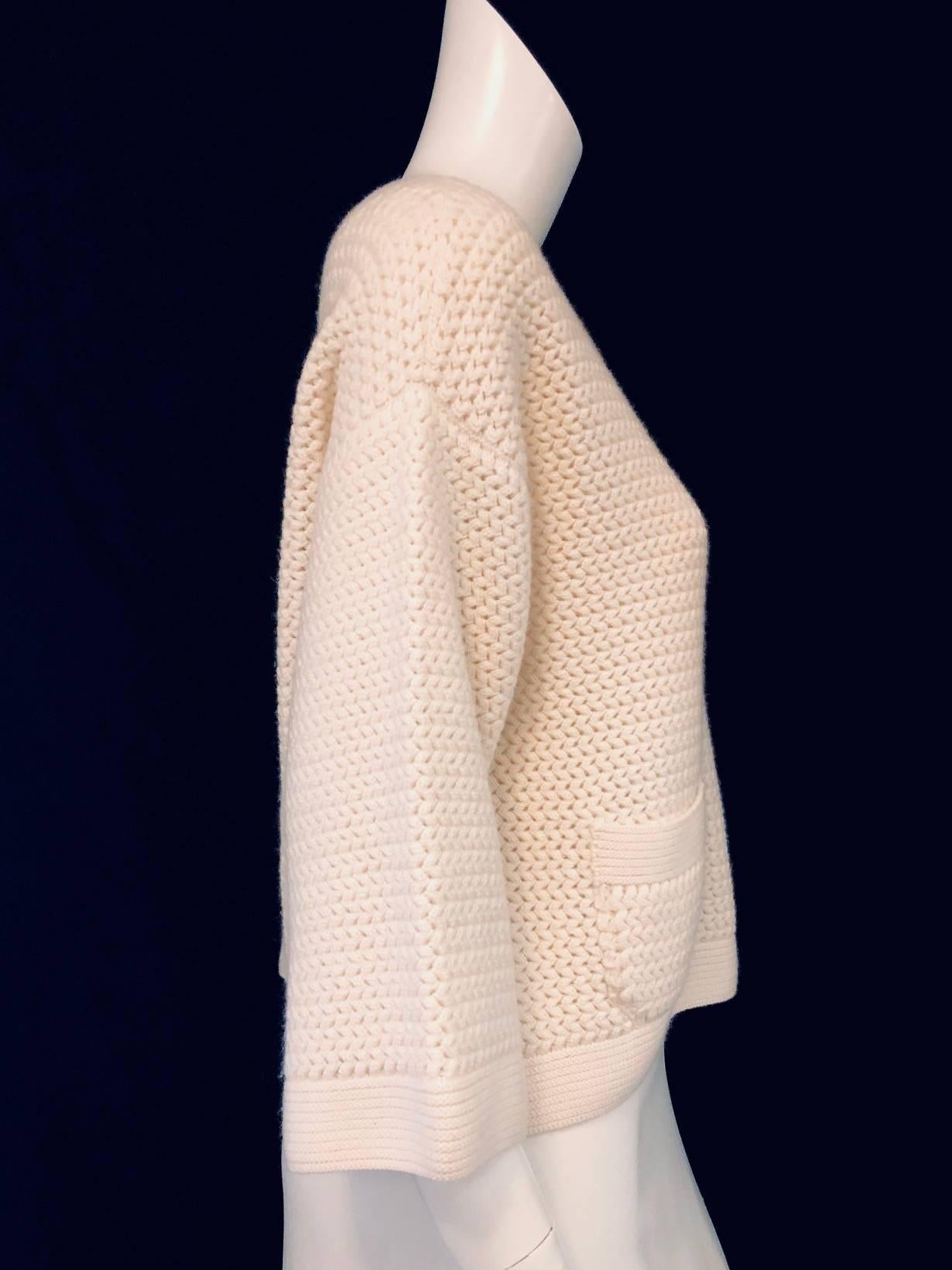 Chanel ivory cashmere crochet sweater features drop shoulders for that relaxed comfy look.  The bateau neckline with ribbed knit around it matches the ribbed knit around the hem and top of patch pockets.  One pocket has an enameled CC button for