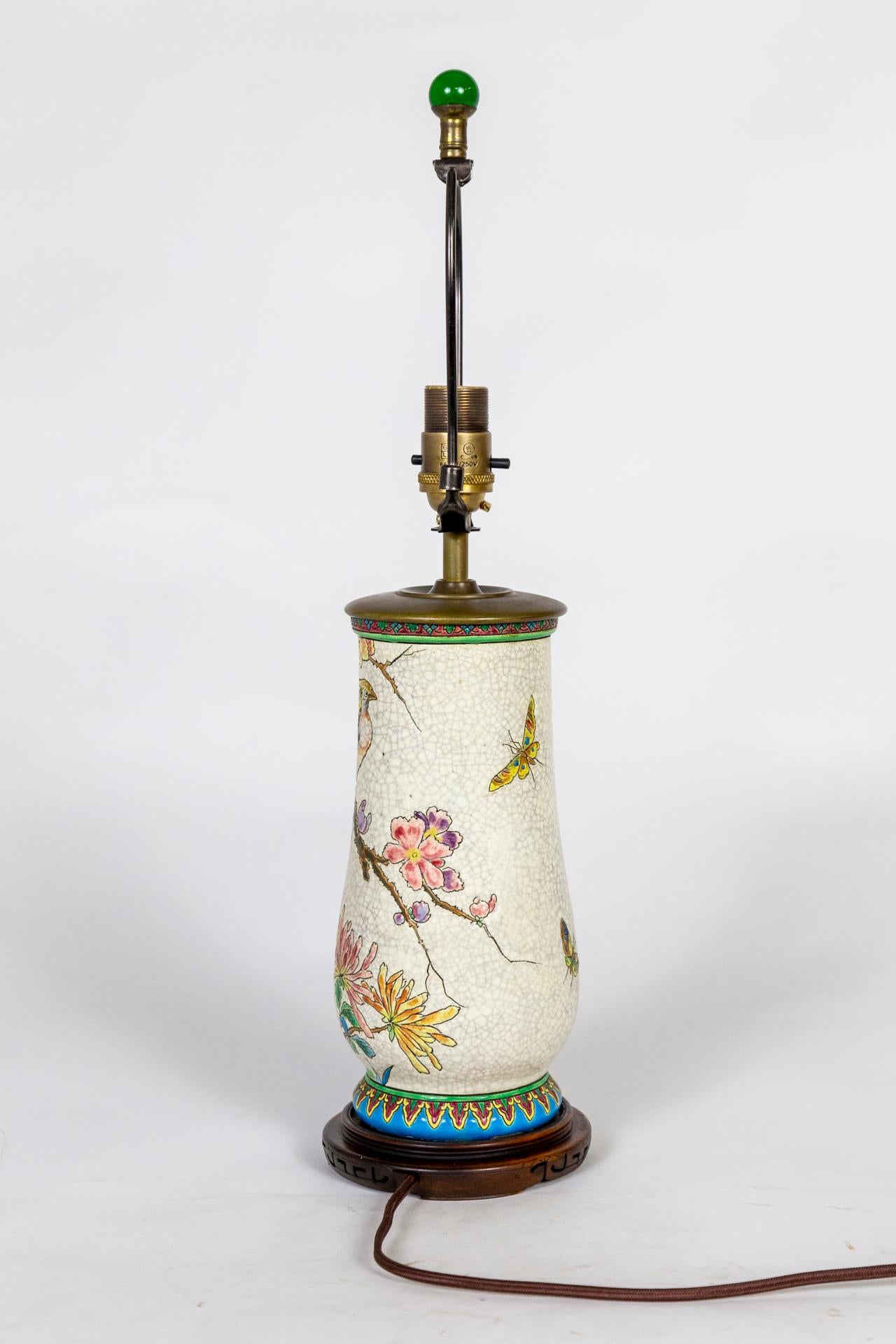 Pièce du Japonisme français du début du 20e siècle, cette lampe de table en céramique blanche émaillée est incisée et peinte à la main de façon complexe avec une scène colorée de paons, de papillons et de fleurs, avec des bordures à motifs. Elle
