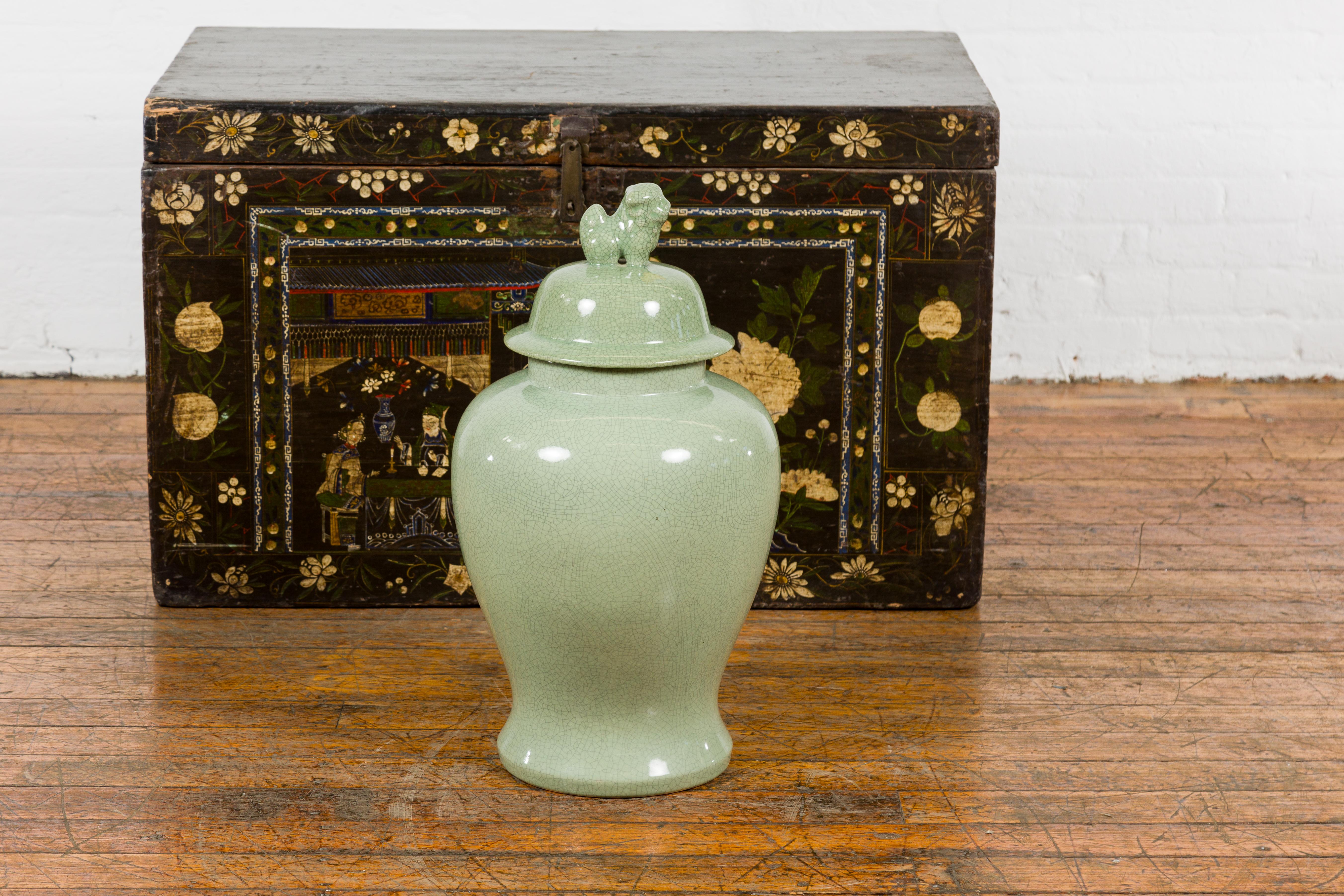 A vintage Chinese crackle green celadon lidded vase from the mid 20th century with stylized foo dog finial and tapering lines. This vintage Chinese crackle green celadon lidded vase, hailing from the mid-20th century, is a captivating testament to