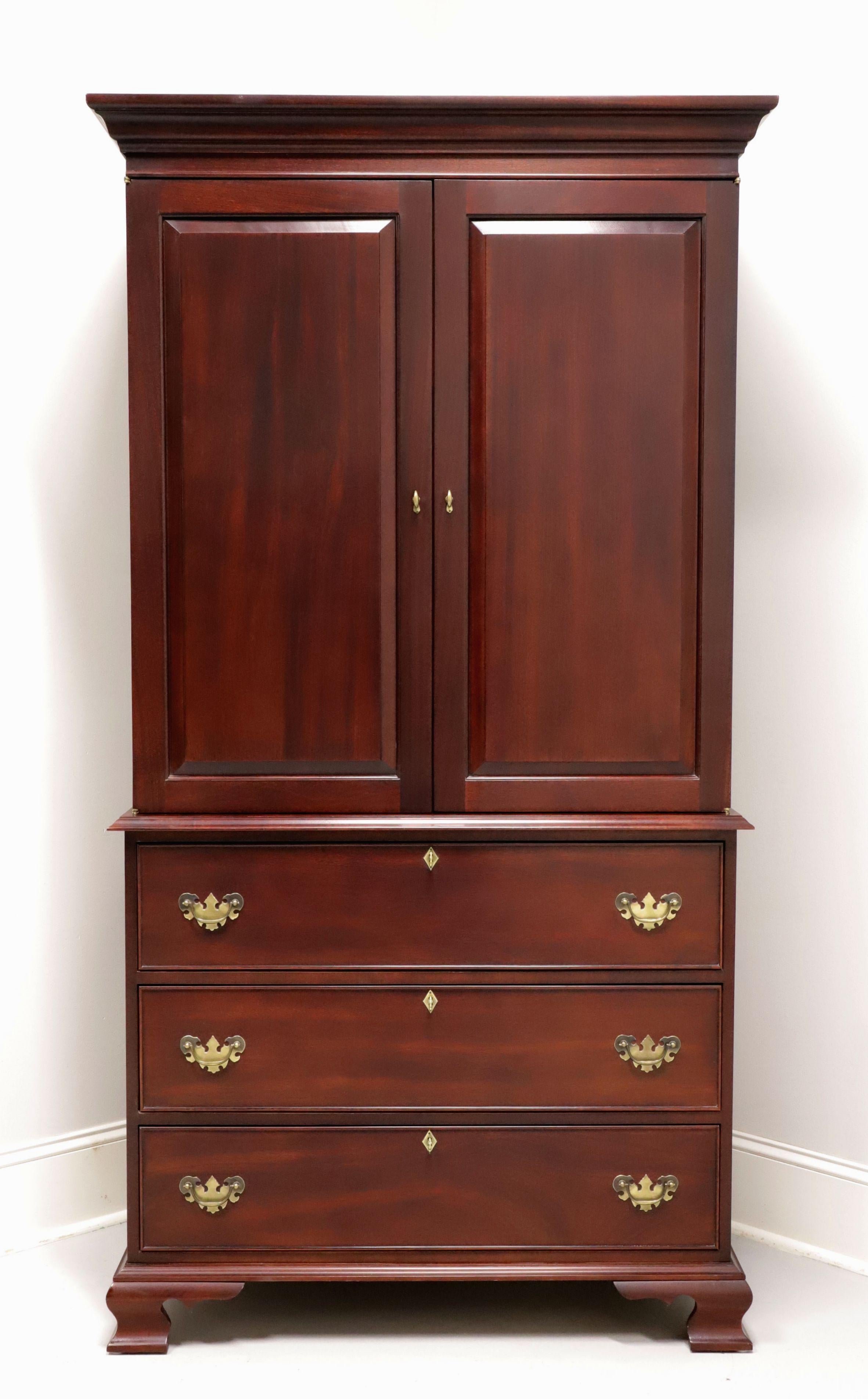A Chippendale style armoire / linen press by high-quality furniture maker Craftique. Custom-crafted of solid mahogany with brass hardware, crown moulding to top, ogee edges, and ogee bracket feet. Upper area features two solid fold flat doors
