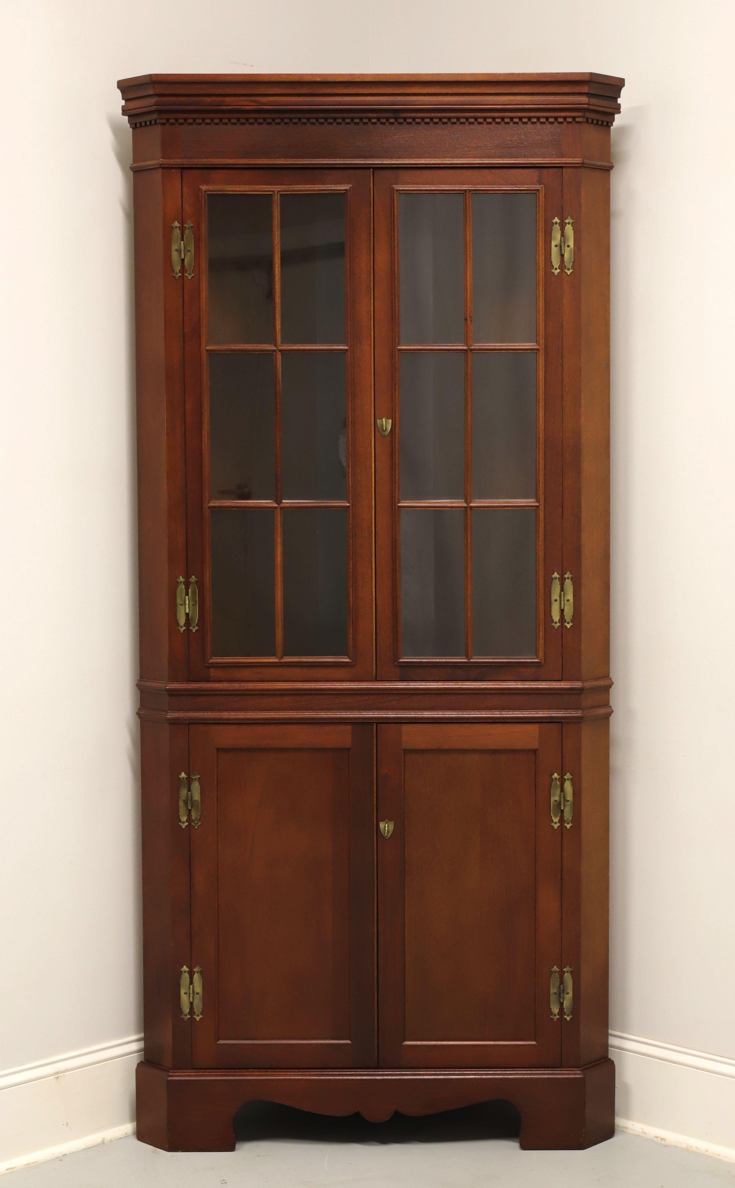 A Chippendale style corner cupboard by high-quality furniture maker Craftique. Solid mahogany with their Old Wood finish, crown & dentil molding to top, carved apron, and bracket feet. Upper cabinet features two fixed plate-grooved wooden shelves