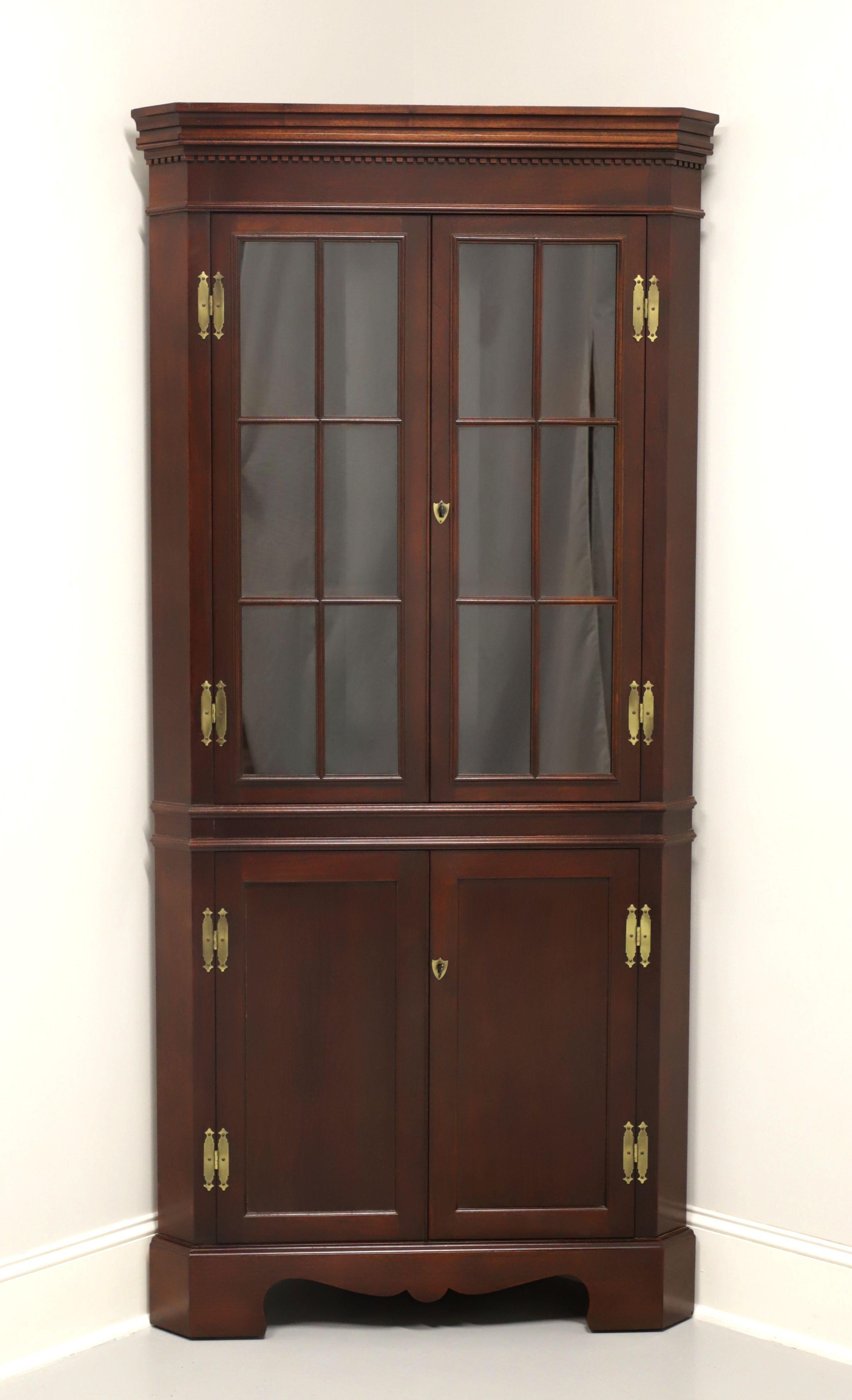 A Chippendale style corner cupboard by high-quality furniture maker Craftique. Solid mahogany with their Old Wood finish, crown & dentil molding to top, carved apron, and bracket feet. Upper cabinet features two fixed plate-grooved wooden shelves