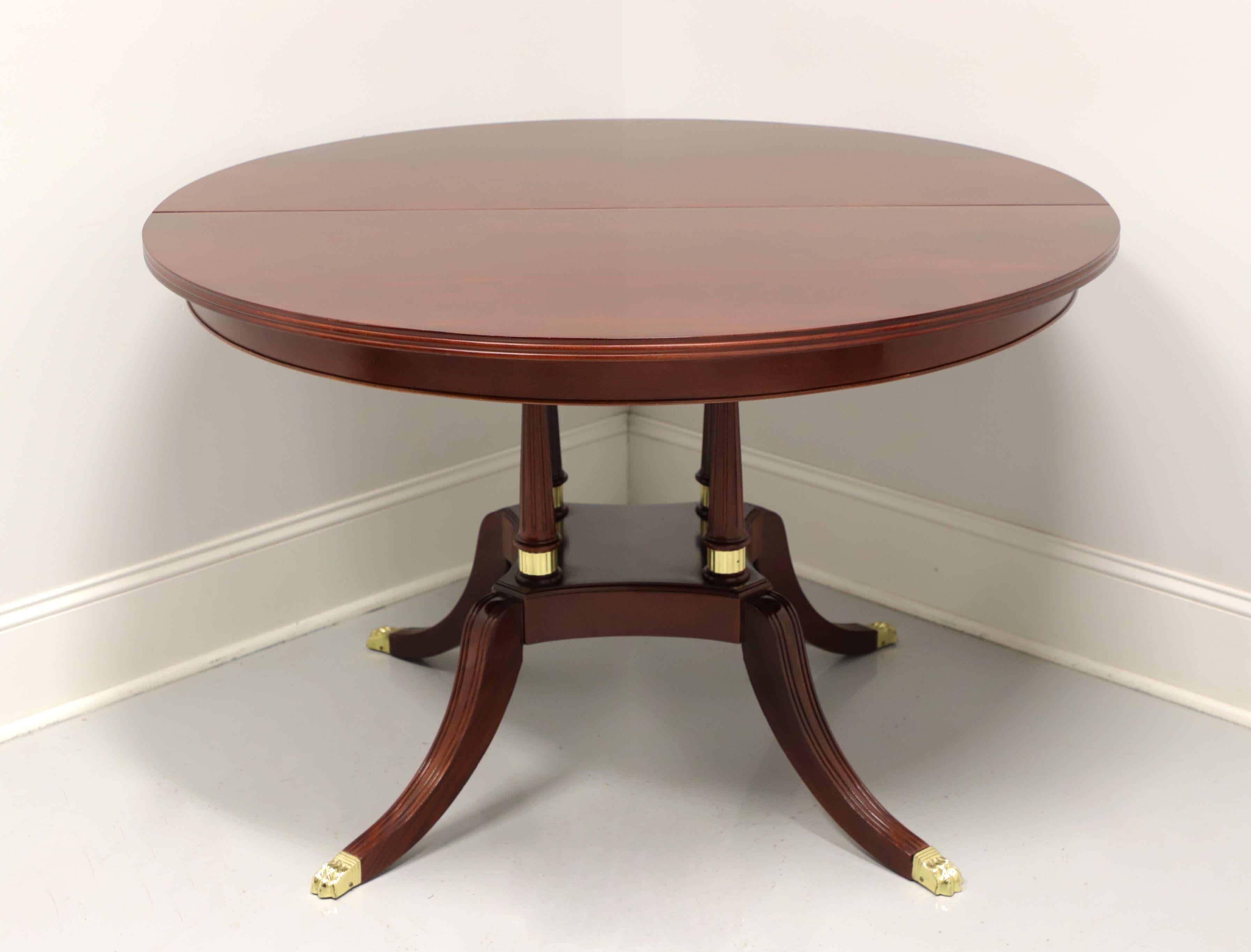 A Regency style dining table by Craftique. Solid mahogany, round to oval top (with leaf), birdcage pedestal with brass accents and four curved legs with brass paw toe caps. Wood expansion sliders with metal gears. Includes one extension leaf. Made