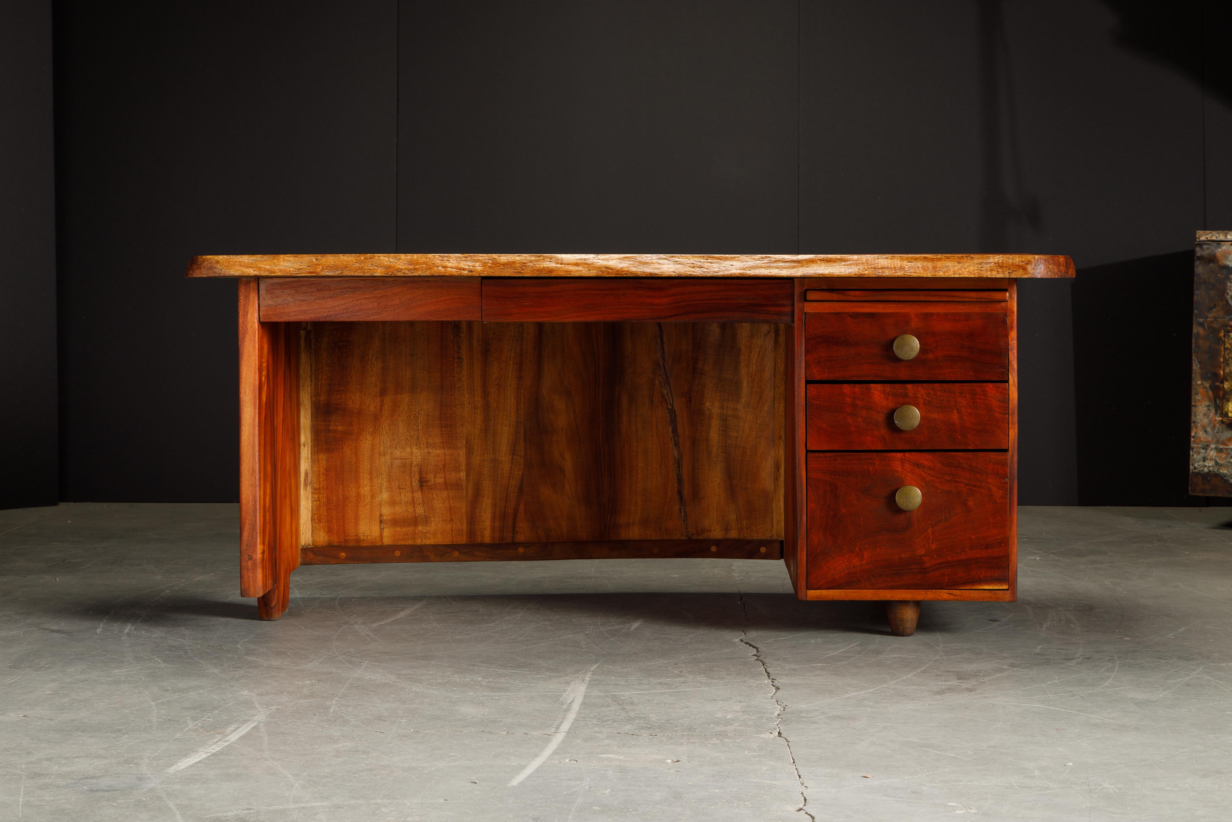 This beautiful 1970s Craftsman desk features a floating double live-edge top, three drawers on the right pedestal along with a center pencil drawer and a pull out writing surface. The wood appears to be an exotic wood, we believe it to be Koa wood.