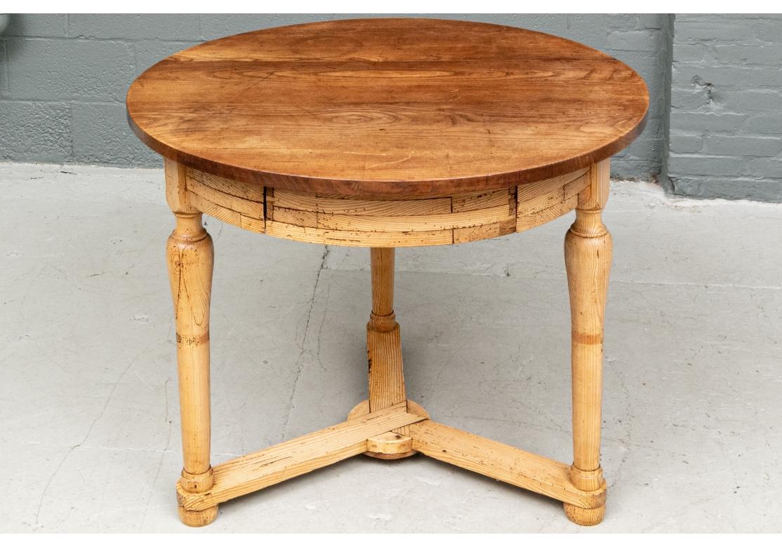 A well made and very decorative circular table constructed of a darker wood plank top mounted on a pale wood base. The apron is made of different shapes in four layers. Raised on three turned legs with inset carved decorative sections. They are