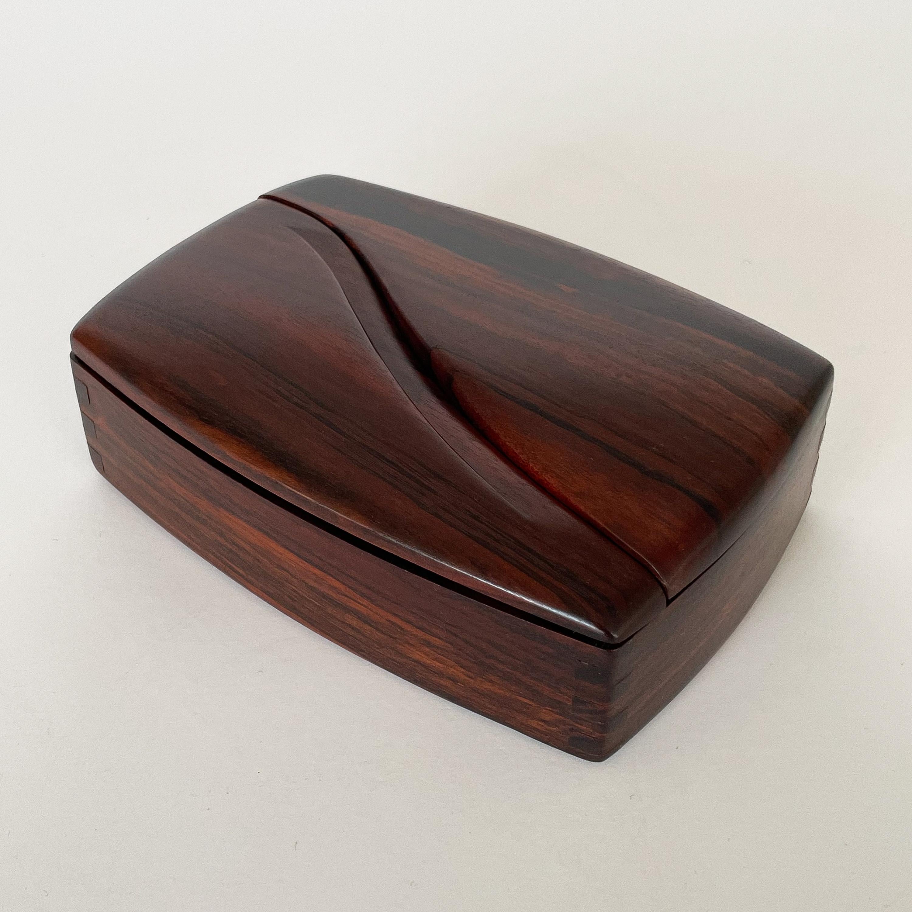 An American Studio Craft carved solid rosewood jewelry / trinket box by Craig Brown, circa 1980s. This modern box features a sculptural split dual swing hinged opening top. Fluid curved shape with beautiful finger joints to corners. Stunning grain