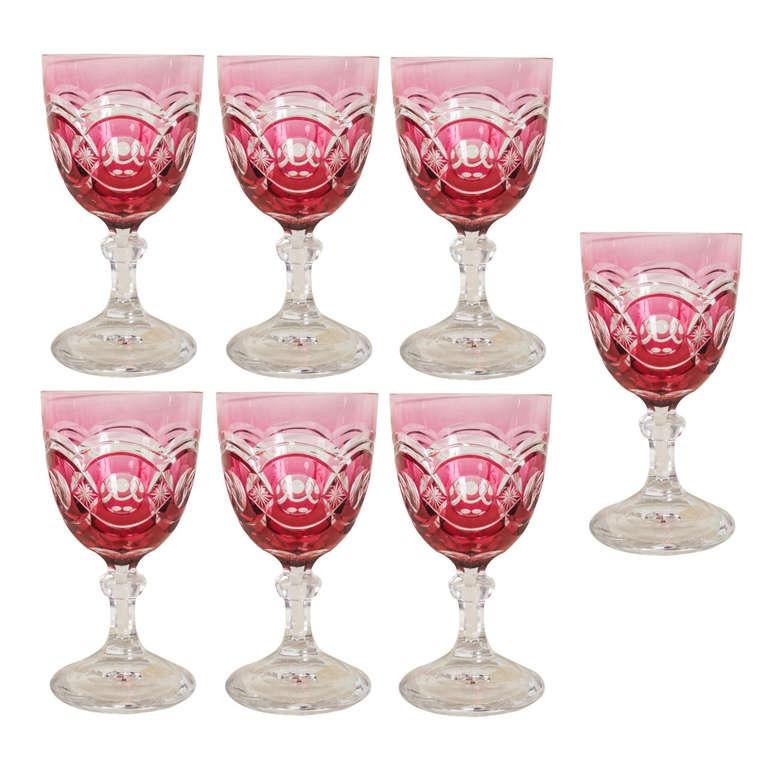 Set of seven (7) heavy cut crystal stemmed glasses/goblets. Each is overlaid in cranberry glass and cut back to clear (cranberry colored glass is created by adding gold to the mixture). The bottoms have large polished pontils.  The color of these