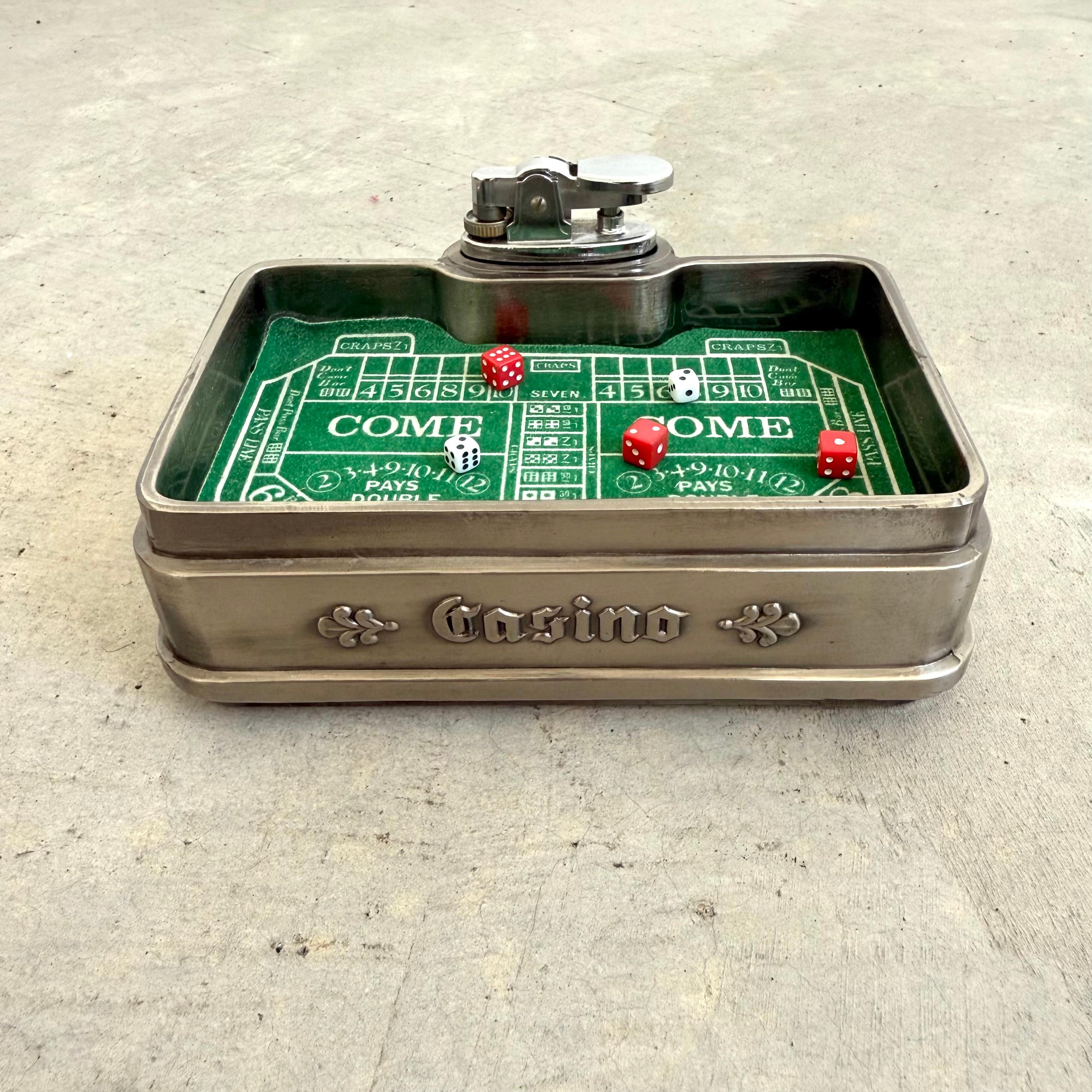 L'accendino da tavolo più bello, a forma di tavolo da Craps. Questo pezzo vintage è curato nei minimi dettagli con dadi sciolti in miniatura bianchi e rossi che si trovano in cima a una tavola di feltro verde. La parola 