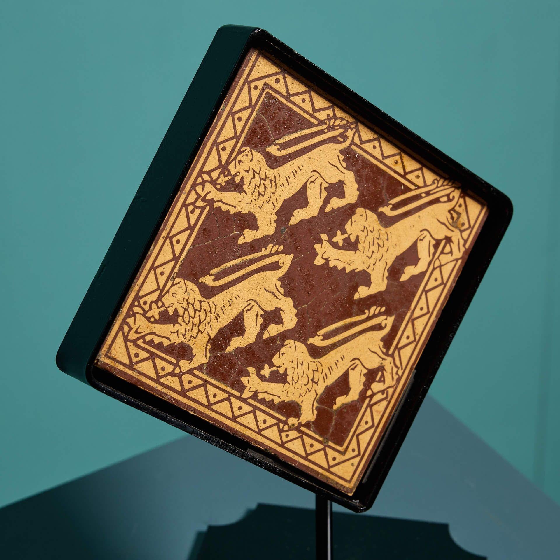A late 19th century encaustic floor tile by Craven Dunhill and Co (stamped) depicting four passant lions in deep red and buff tones. This 6-inch tile includes a bespoke steel stand as pictured, making it a stunning decorative interior piece for