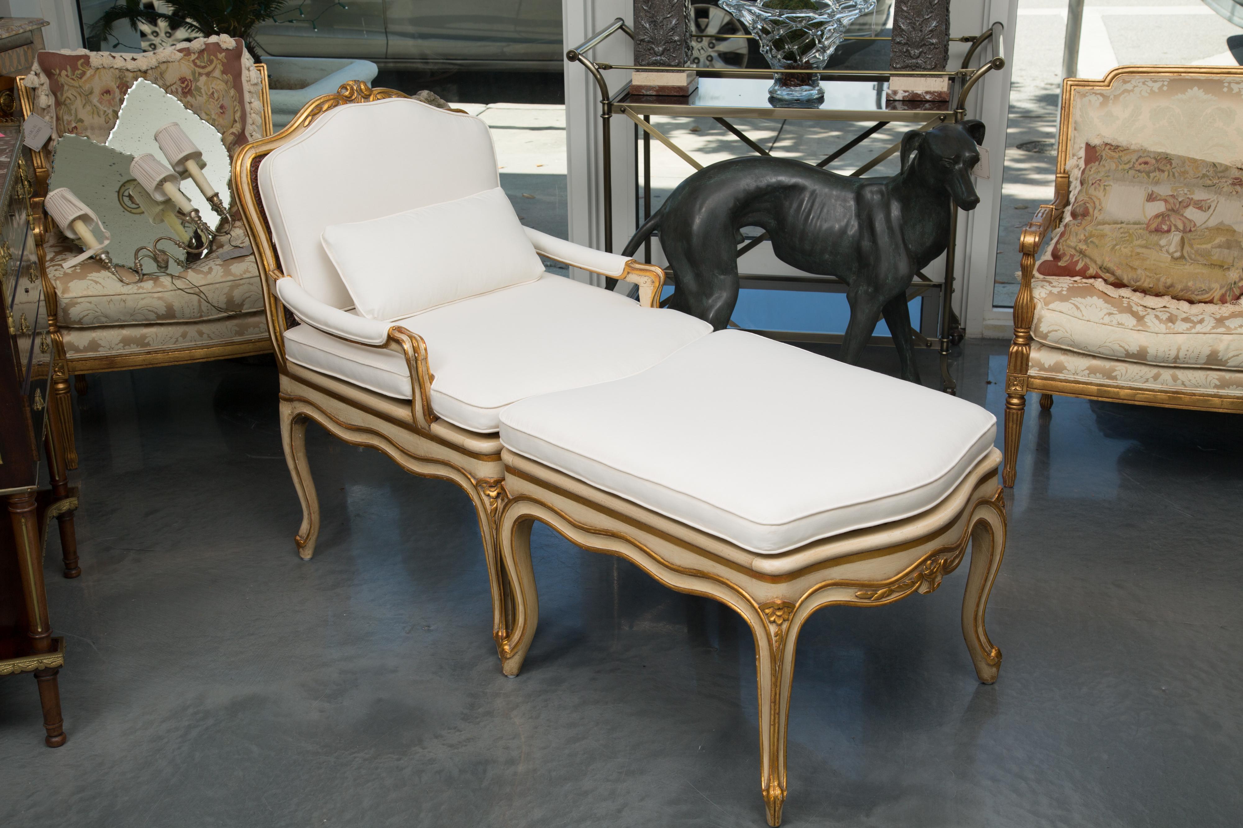 This is lovely cream painted and parcel gilt duchess brisee with cane insets on the back and seat of the arm chair and cane inset on the seat of the ottoman, circa early 20th century.