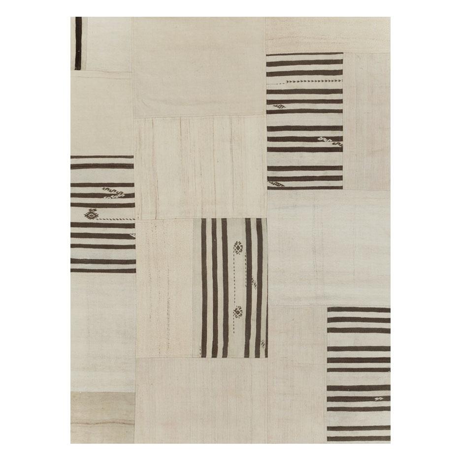 A contemporary Turkish flatweave Kilim large room size carpet handmade during the 21st century in shades of cream and black. This patchwork style rug consists of hand-weaving together several remnants of vintage Kilim carpets from the mid-20th