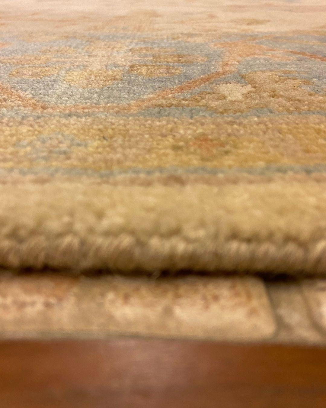 Dieser cremefarbene, blaue und erdfarbene Oushak-Teppich mit Blumenmotiven in den Maßen 6' x 9' verkörpert die schlichte Eleganz der traditionellen Weberei. Das zart cremefarbene Feld dient als ruhiger Hintergrund für komplizierte botanische Muster,
