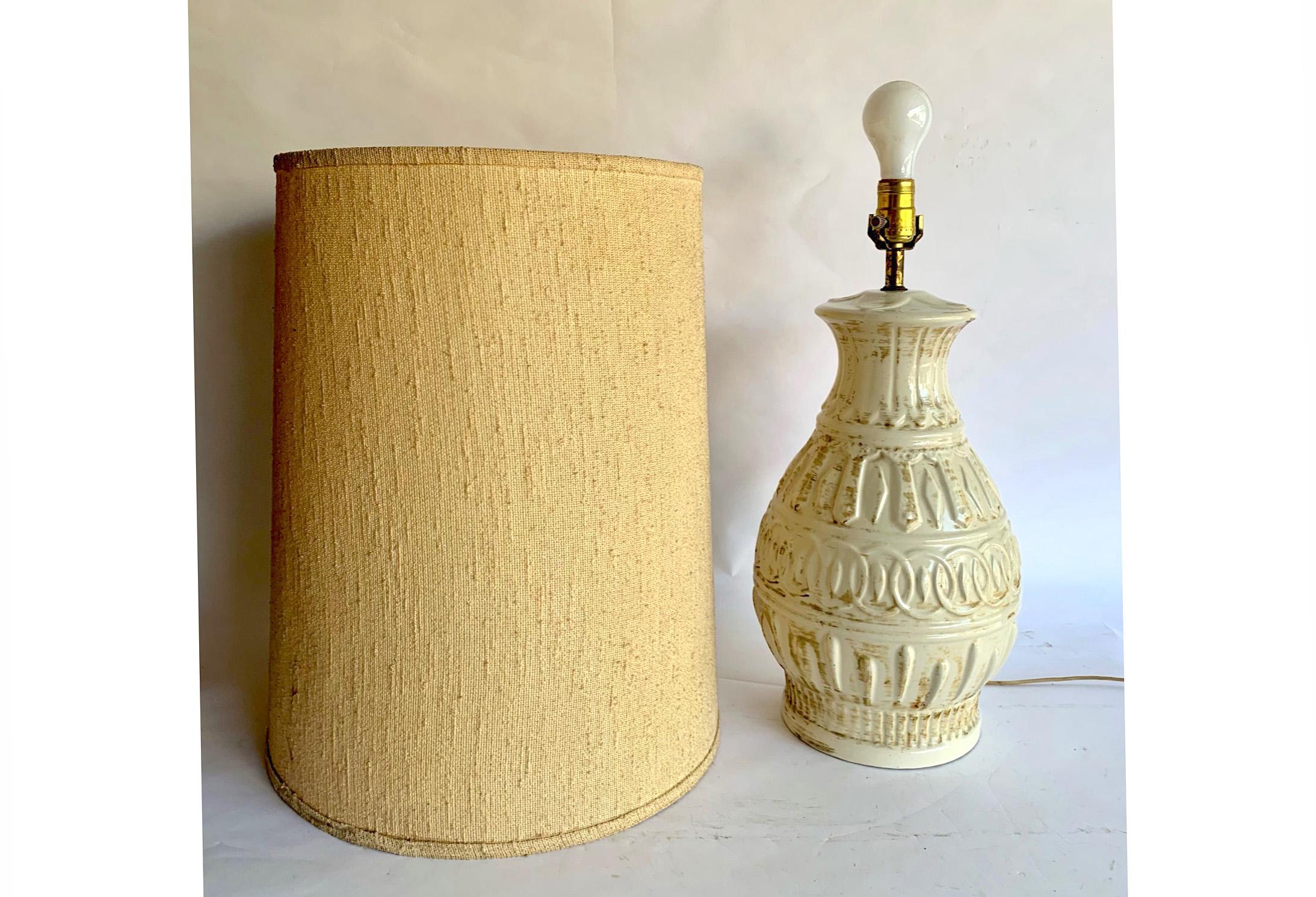 Striking table lamp made of cream colored ceramic with a brushed brown glaze. Pattern in relief includes chainlink circles and darts. Includes original tan, nubby shade.

Very good vintage condition. No cracks or damage to ceramic. Very clean. Shade