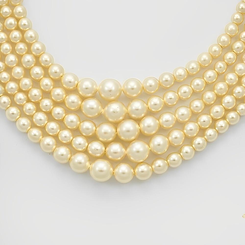 Collier de fausses perles de couleur crème, avec cinq rangs de perles graduées. Il est doté d'un joli fermoir en strass. Longueur intérieure 40,5 cm.

Ce magnifique collier vintage classique serait fabuleux porté lors d'un mariage ou d'une occasion
