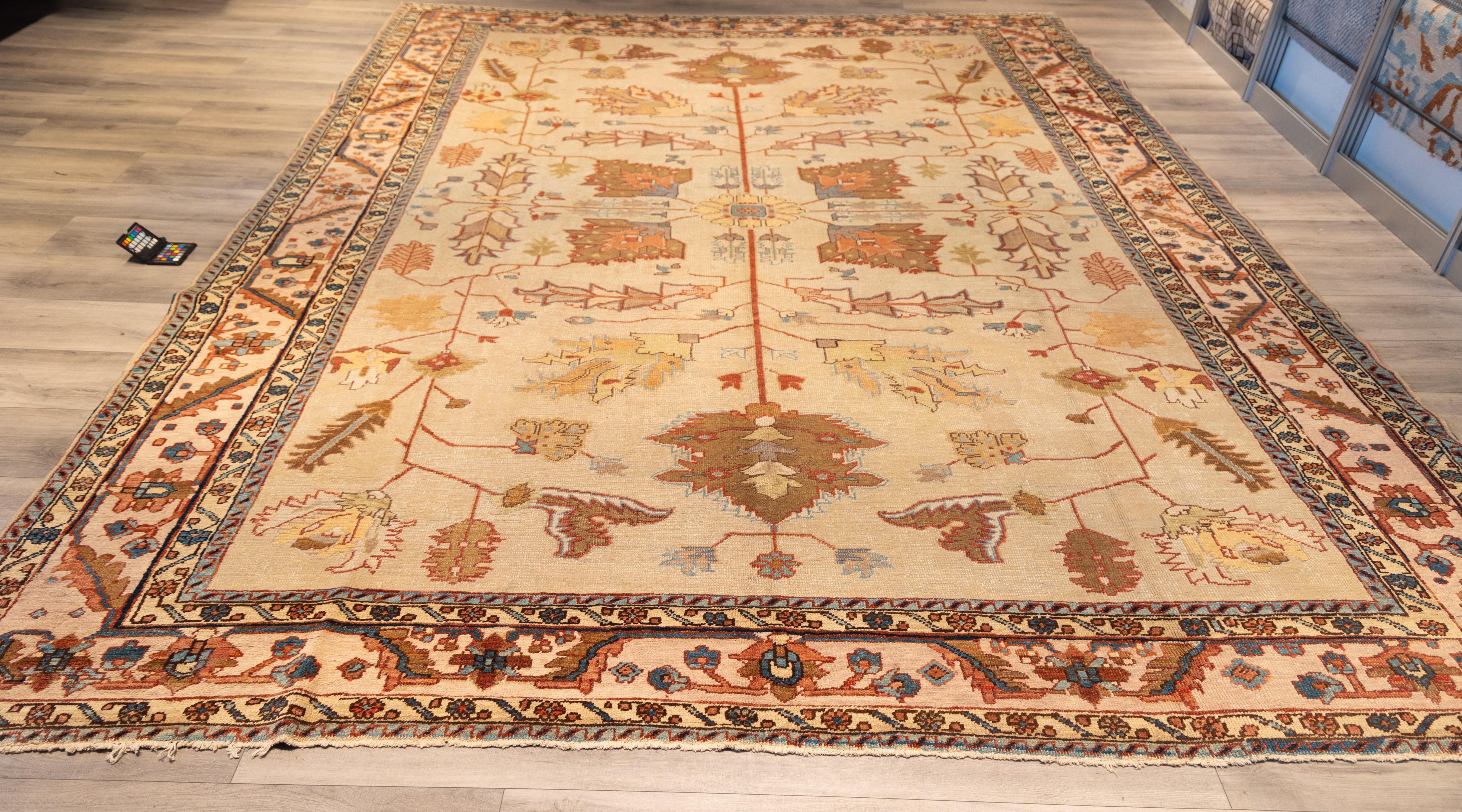 Featuring a refined and symmetric allover design centered around a tree-of-life or floral schematic. The soft ivory ground is adorned with stylized botanical motifs in tones of terracotta, rust, soft gold, and muted gray-blue. The composition is