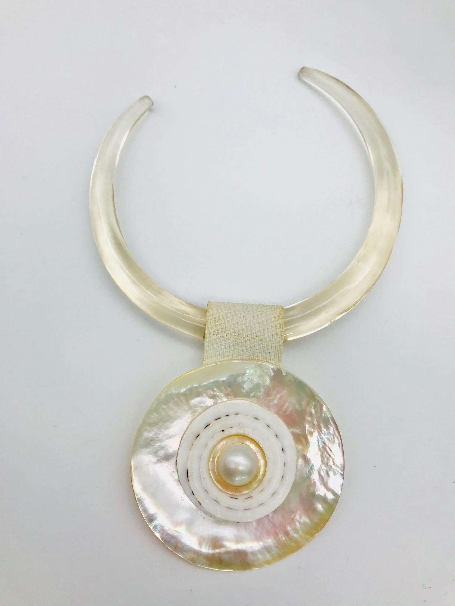 This pendant consists of a large  Mabe Pearl framed in French Deco ring   on top of a white Mother of pearl with exceptional iridescence. Pendant  is attached to the clear resin choker by a white rubber strap. The image of this Mabe pearl is in the
