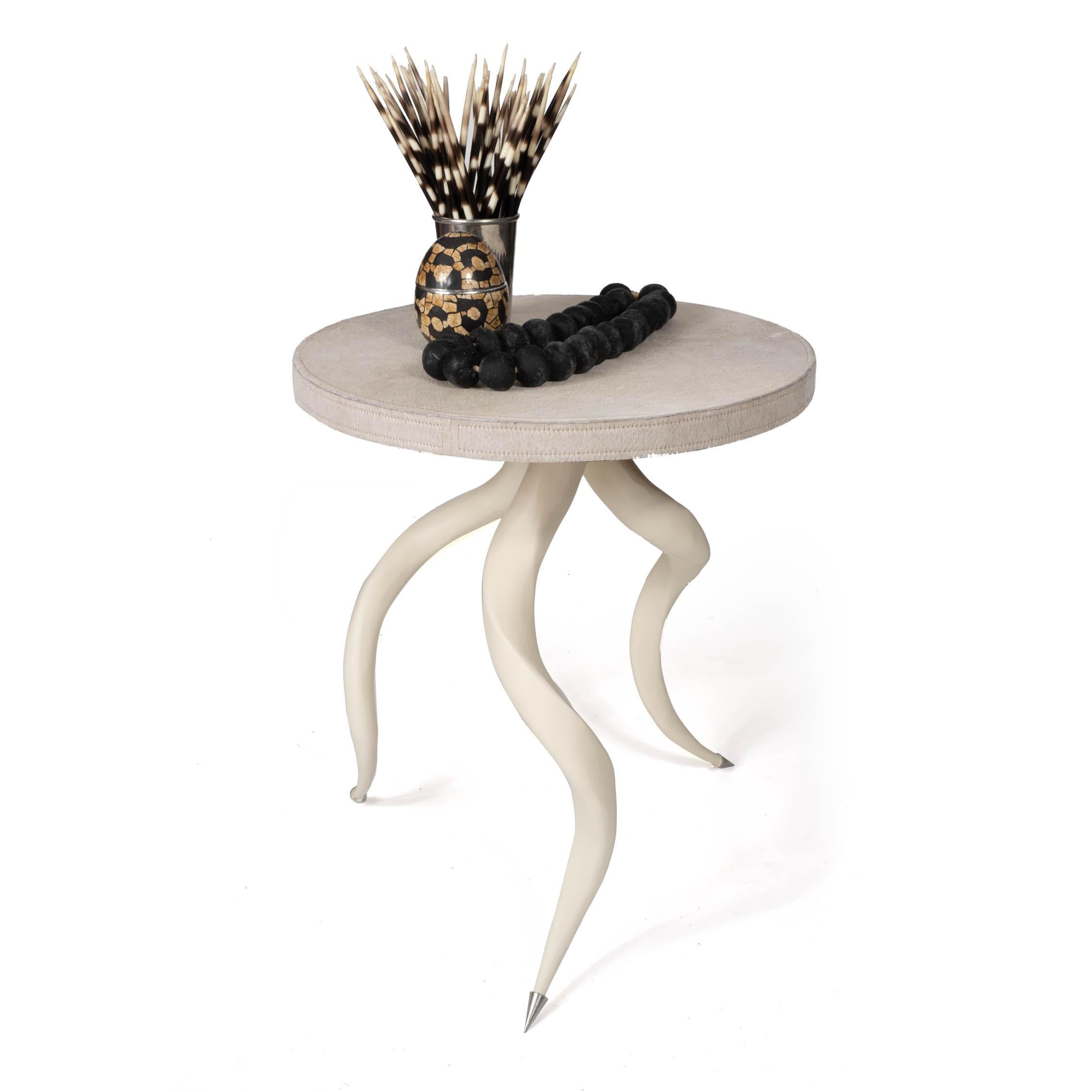 Esta mesa auxiliar, un complemento naturalmente lujoso para cualquier habitación, está colocada sobre un trío de cuernos de kudú de origen sostenible, pulidos y rociados, con un tablero de auténtica piel de vaca. Debido al uso de materiales