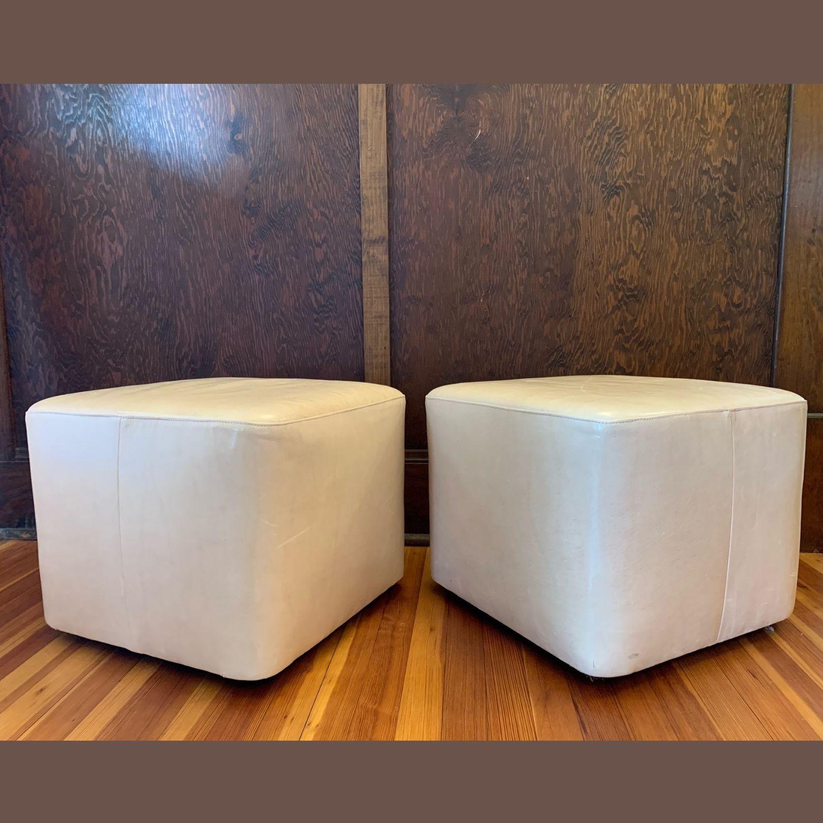This contemporary pair of buttery-soft leather ottomans can be used either as extra seating or a comfortable foot rest in a living room, bedroom, or den. Done in a cream-colored, almost pink leather, each seat sits on four recessed brass castors,