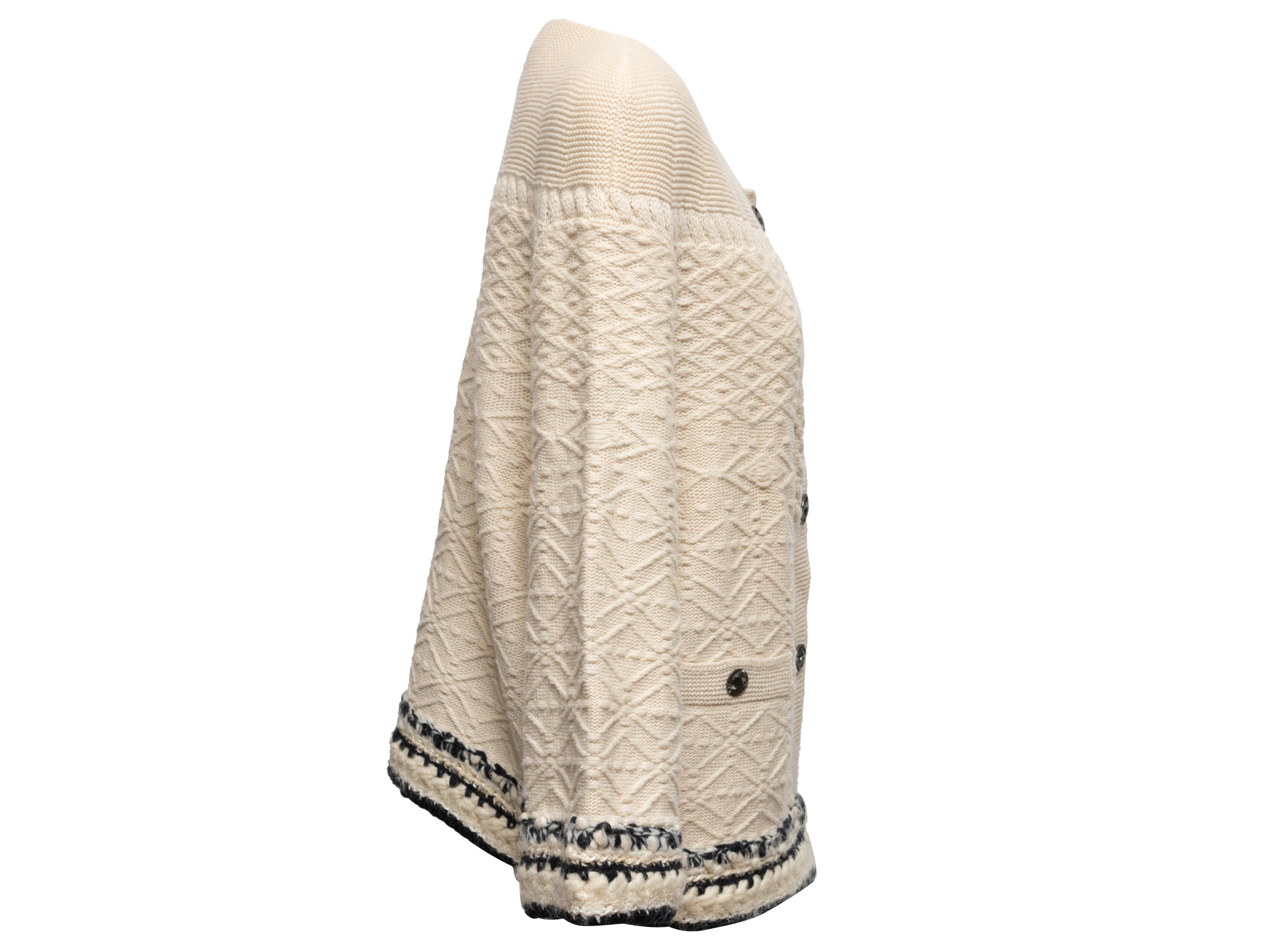 Cream and navy textured cashmere cardigan by Chanel. Crew neck. Fringe trim. Dual hip pockets. Button closures at center front. 46