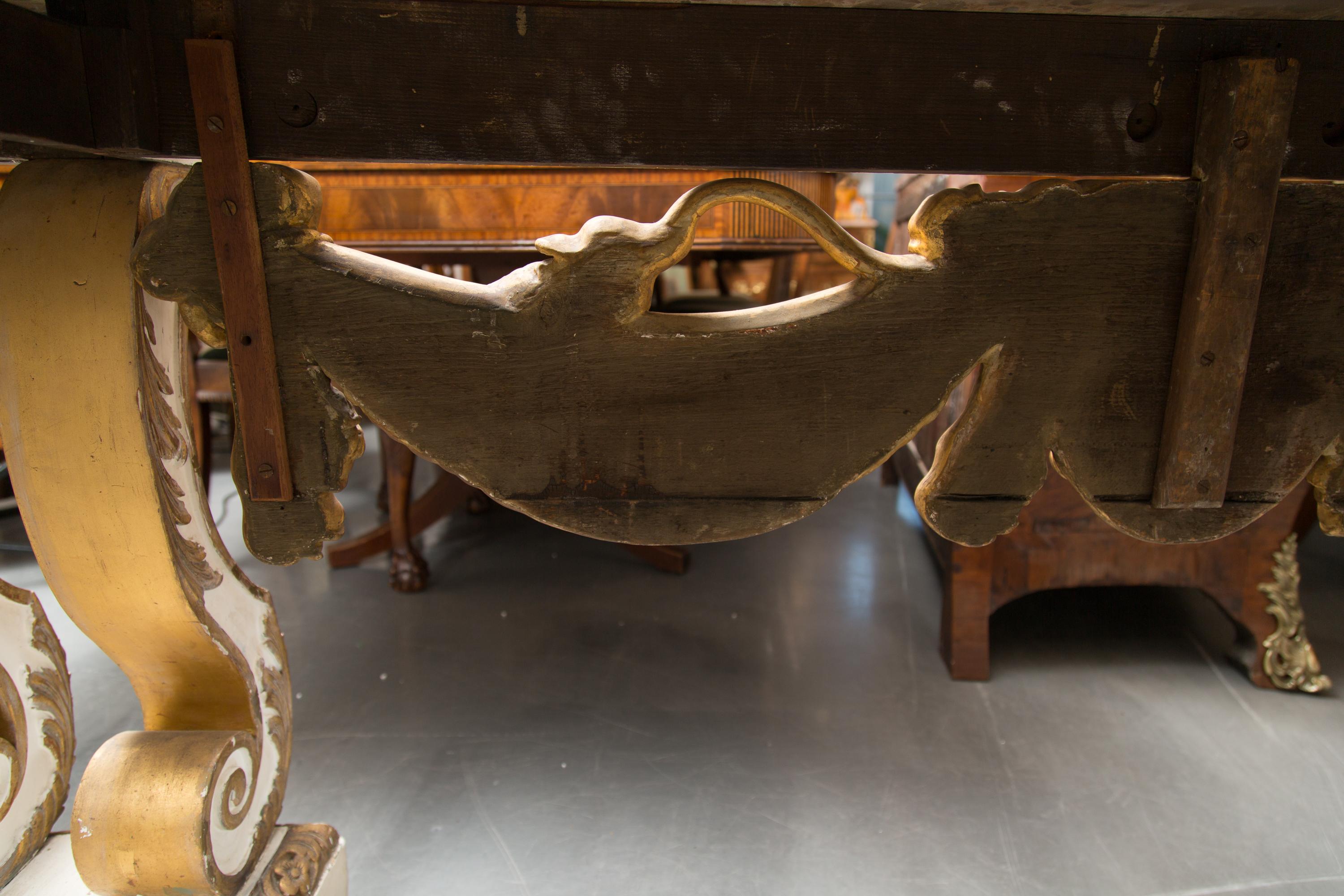 This is an impressive and large-scale cream-painted and parcel gilt console table. The rouge variegated marble top is above a central ornamentation of a lion mask flanked by bold drapery-form swags. The entirety of the console is supported by a