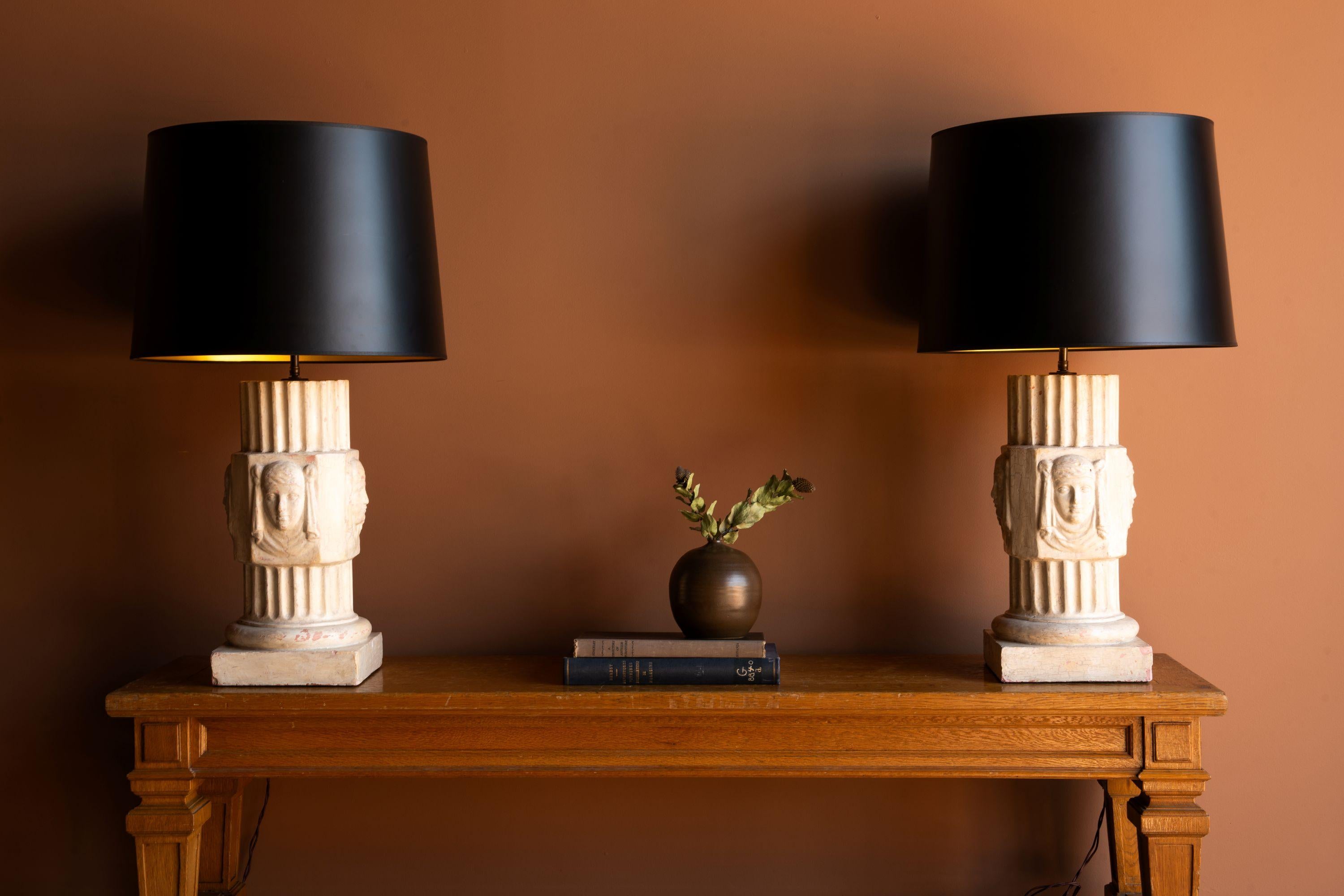 Paire de lampes en plâtre au design classique frappant, ressemblant à une colonne architecturale avec des visages sculptés en relief. La colonne présente des détails cannelés et est montée sur une base carrée, ce qui lui confère une présence solide