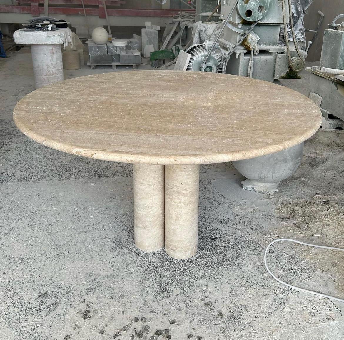 Dieser minimalistische Tisch aus massivem Travertin verfügt über eine runde Tischplatte mit geschwungener Kante, die elegant auf drei zylindrischen Säulen ruht. 

Die Säulenbeine, die von den Vintage-Stücken von Mario Bellini inspiriert sind,