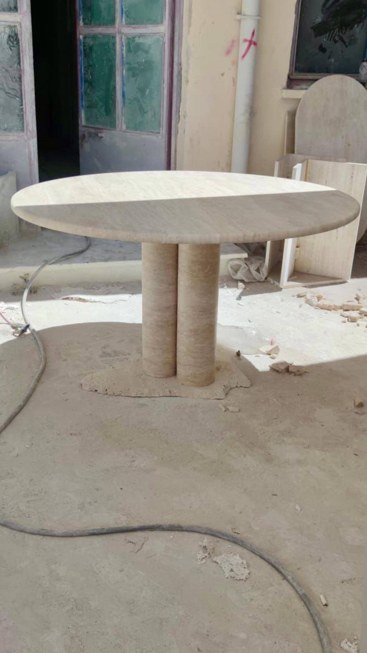 Cette table minimaliste est fabriquée en travertin massif, avec un plateau circulaire au bord incurvé qui repose élégamment sur trois colonnes cylindriques. 

S'inspirant des pièces vintage de Mario Bellini, les pieds en colonne donnent à cette