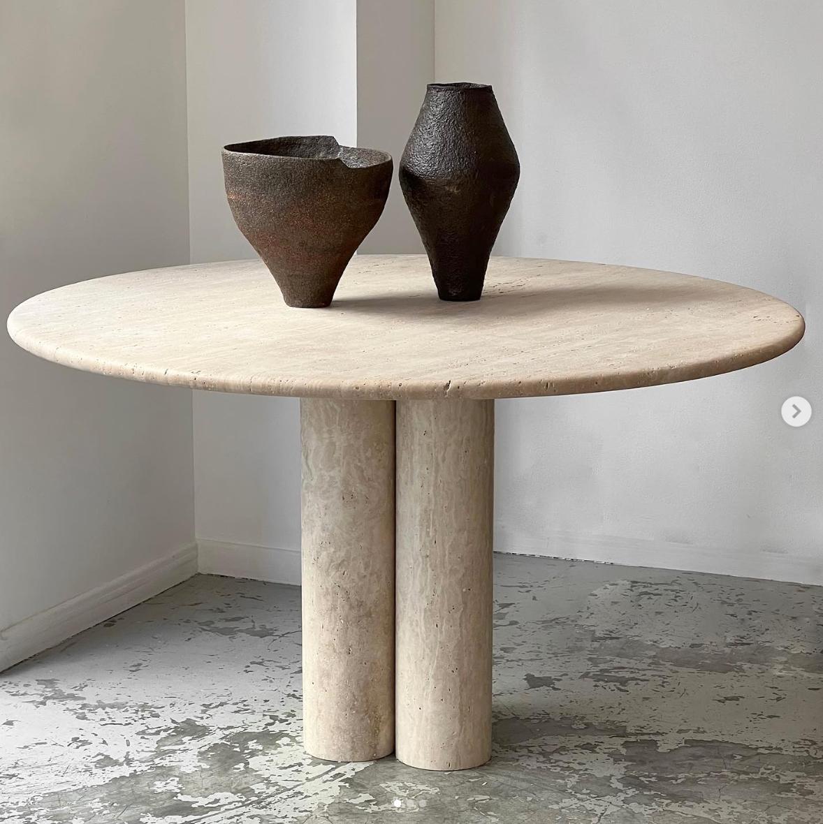 This minimalist table is made from solid travertine, featuring a circular table top with a curved edge that elegantly sits on three cylindrical columns. 

Drawing inspiration from the vintage pieces of Mario Bellini, the column legs give this table